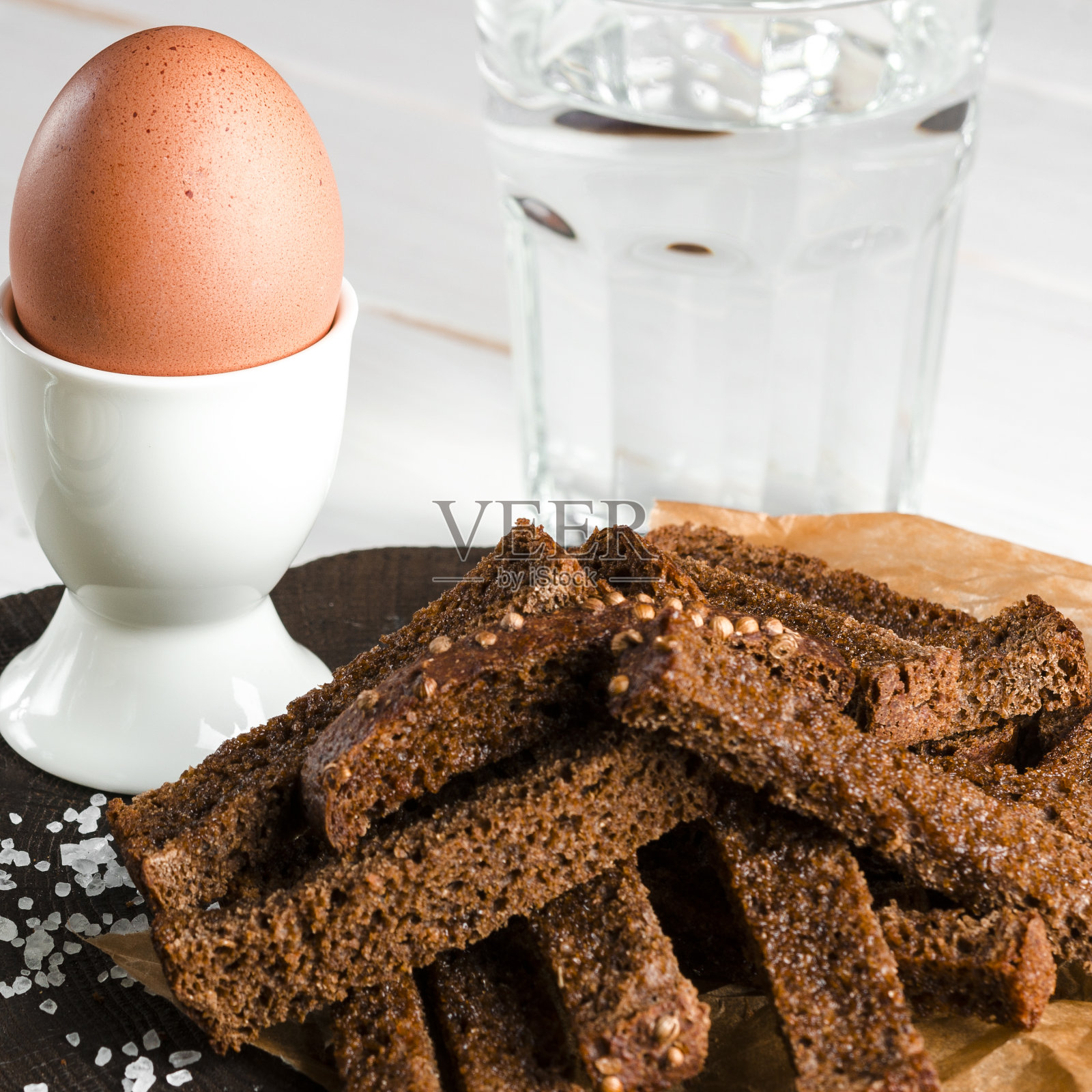 健康食品。木桌上放着一个放在白色陶瓷架子上的煮鸡蛋,旁边是黑麦面包丁和白酱汁照片摄影图片
