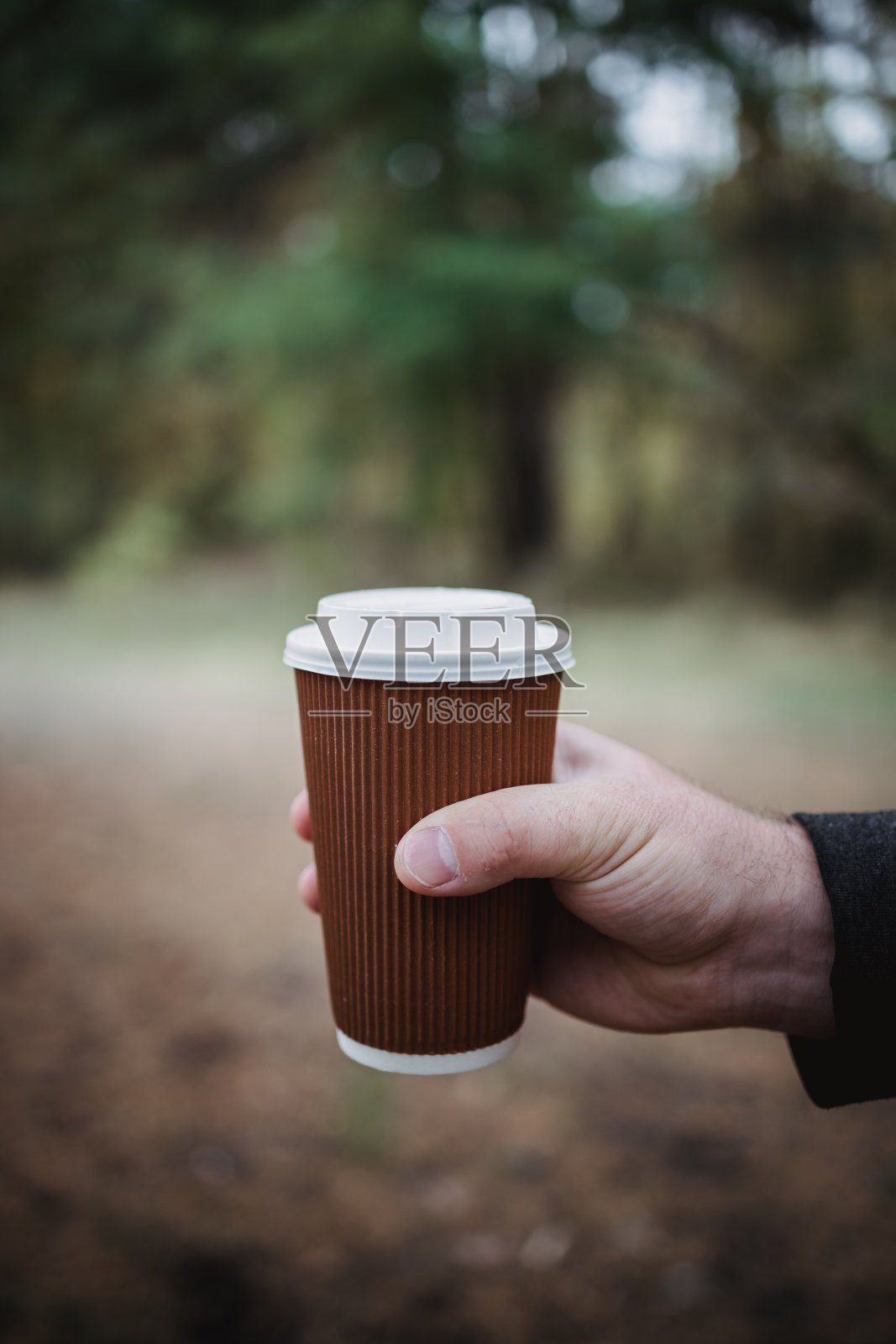 在秋叶的背景下,一个男人拿着一个外卖纸板玻璃,上面放着茶和咖啡。温暖的秋色气氛,柔和的焦点。本空间照片摄影图片