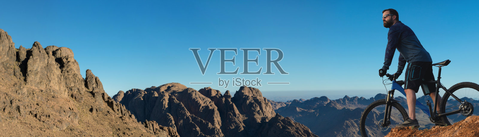 骑自行车的人穿着短裤和运动衫,骑着带有空气悬挂叉的现代碳硬尾自行车征服山峰。从山上看,美丽的景色。照片摄影图片