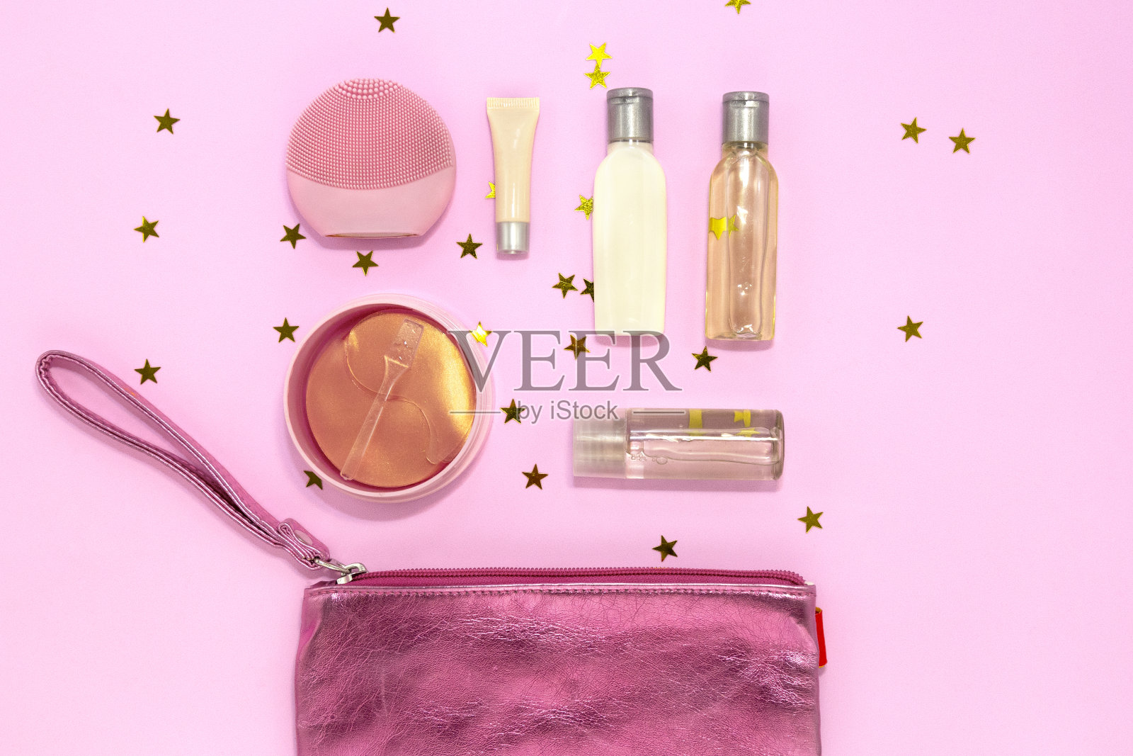 化妆包与化妆产品-硅胶洁面刷,水凝胶眼罩,罐子和瓶子与霜和凝胶在粉红色的背景与金色星星。平躺,俯视图。照片摄影图片