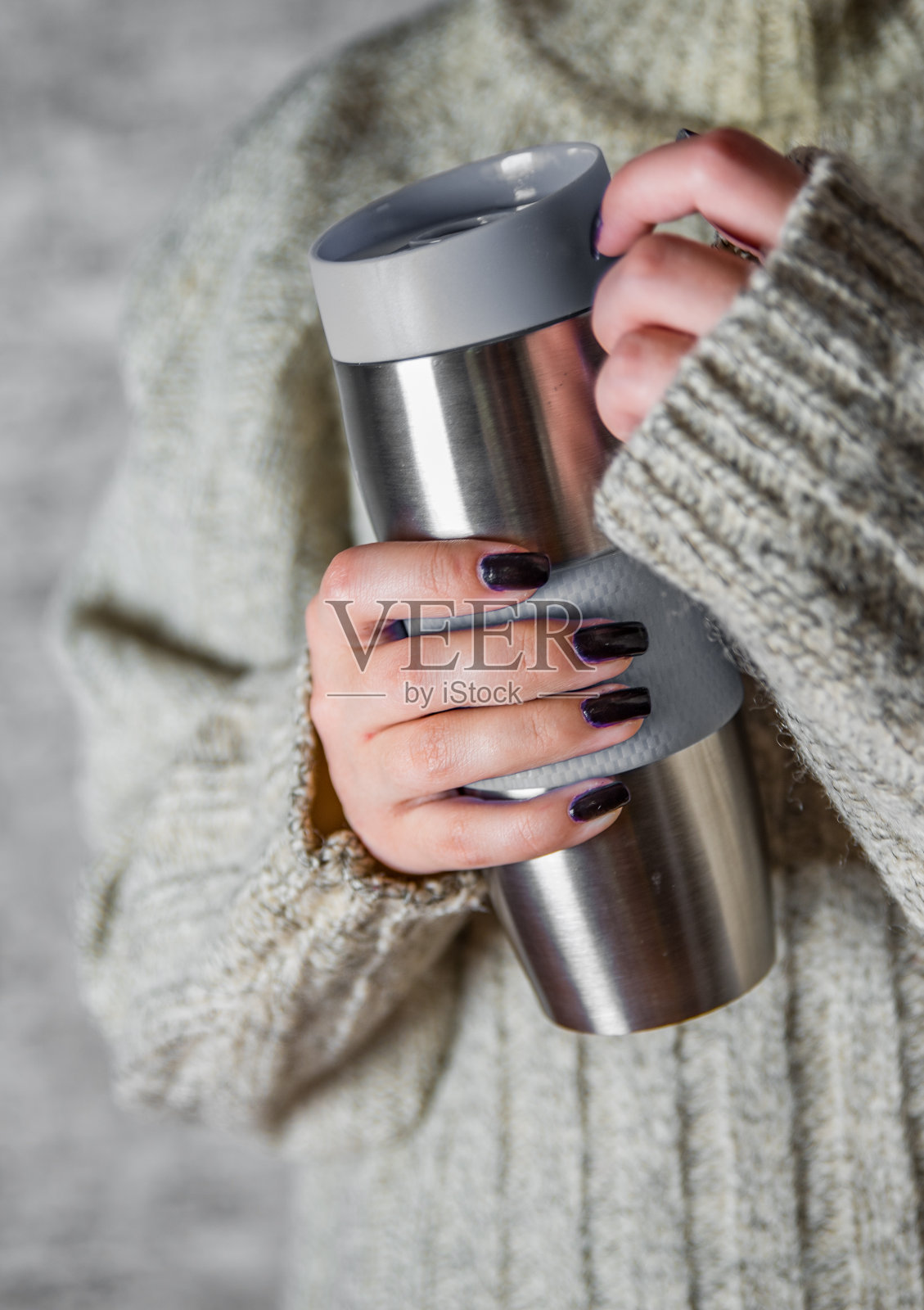 穿着毛衣的女人拿着一个温度计,手里拿着一杯热饮,放在灰色的墙壁上照片摄影图片