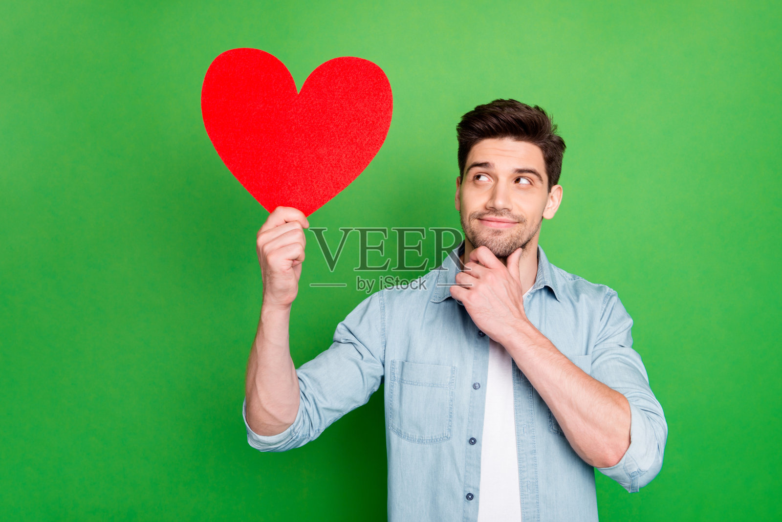 照片惊人的家伙拿着大红纸心思考舞会邀请女朋友有好想法穿牛仔衬衫孤立的绿色背景照片摄影图片