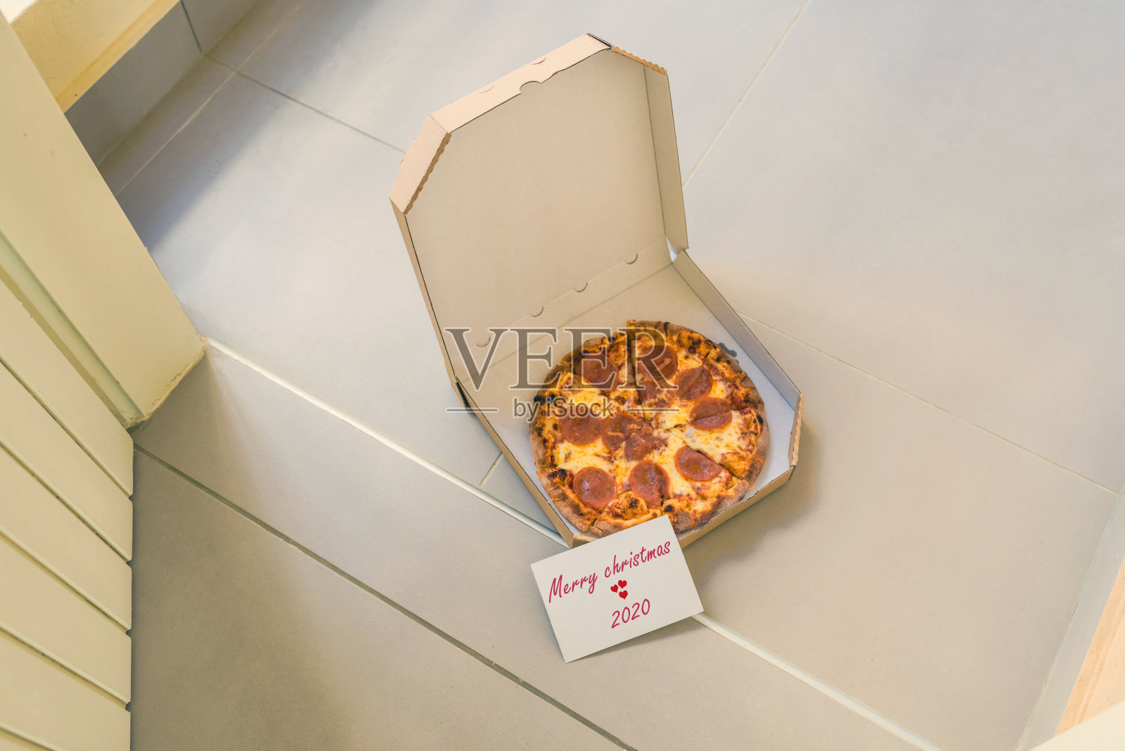 打开一盒披萨和写着2020年圣诞快乐的卡片放在家门口的门廊上。交付。概念照片摄影图片
