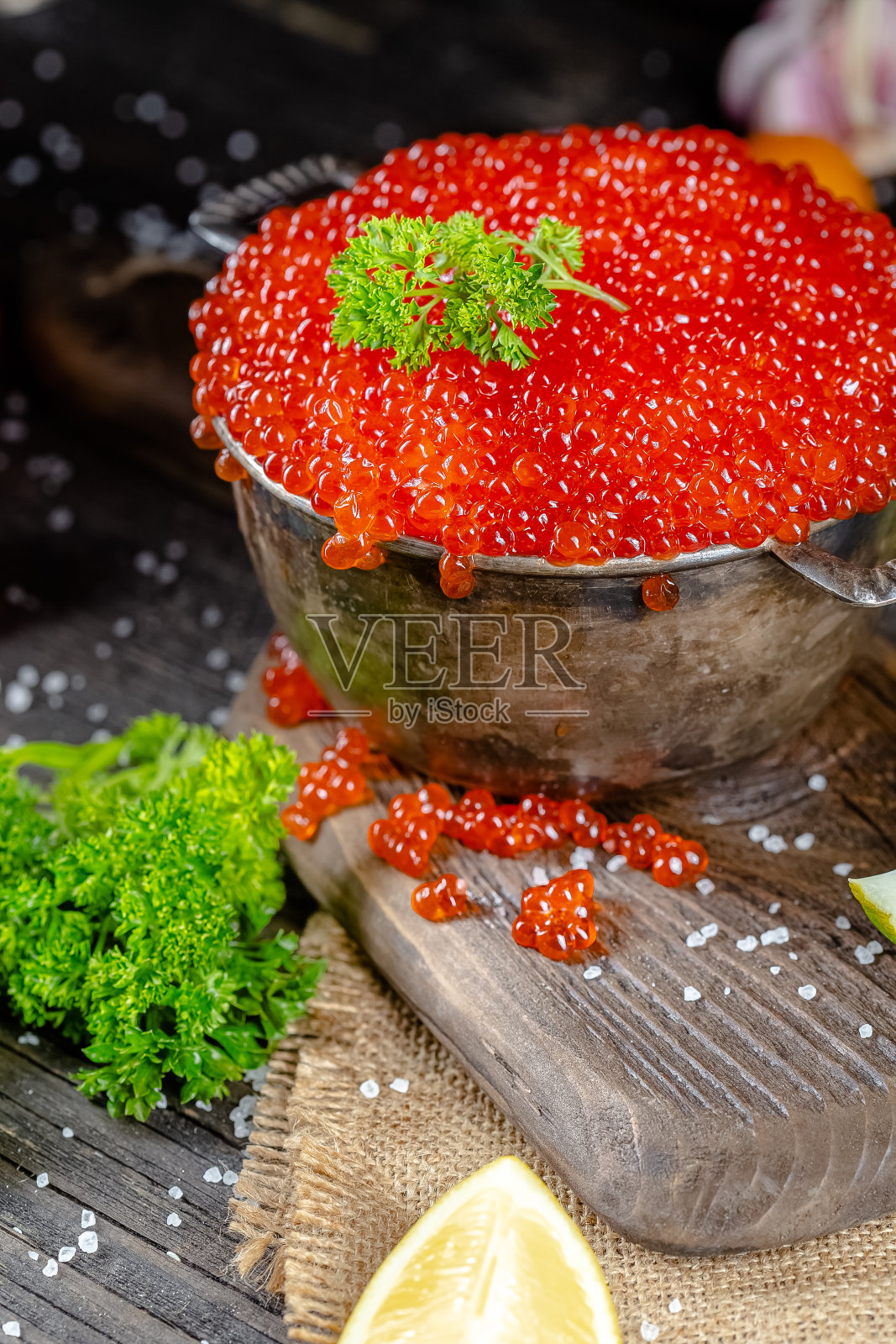 乡村复古风格的大红鱼子酱,一大碗深桶炖锅,放在木砧板和桌子上,上面有绿色蔬菜、蔬菜、柠檬和酸橙,大海盐,深色,从上到下照片摄影图片