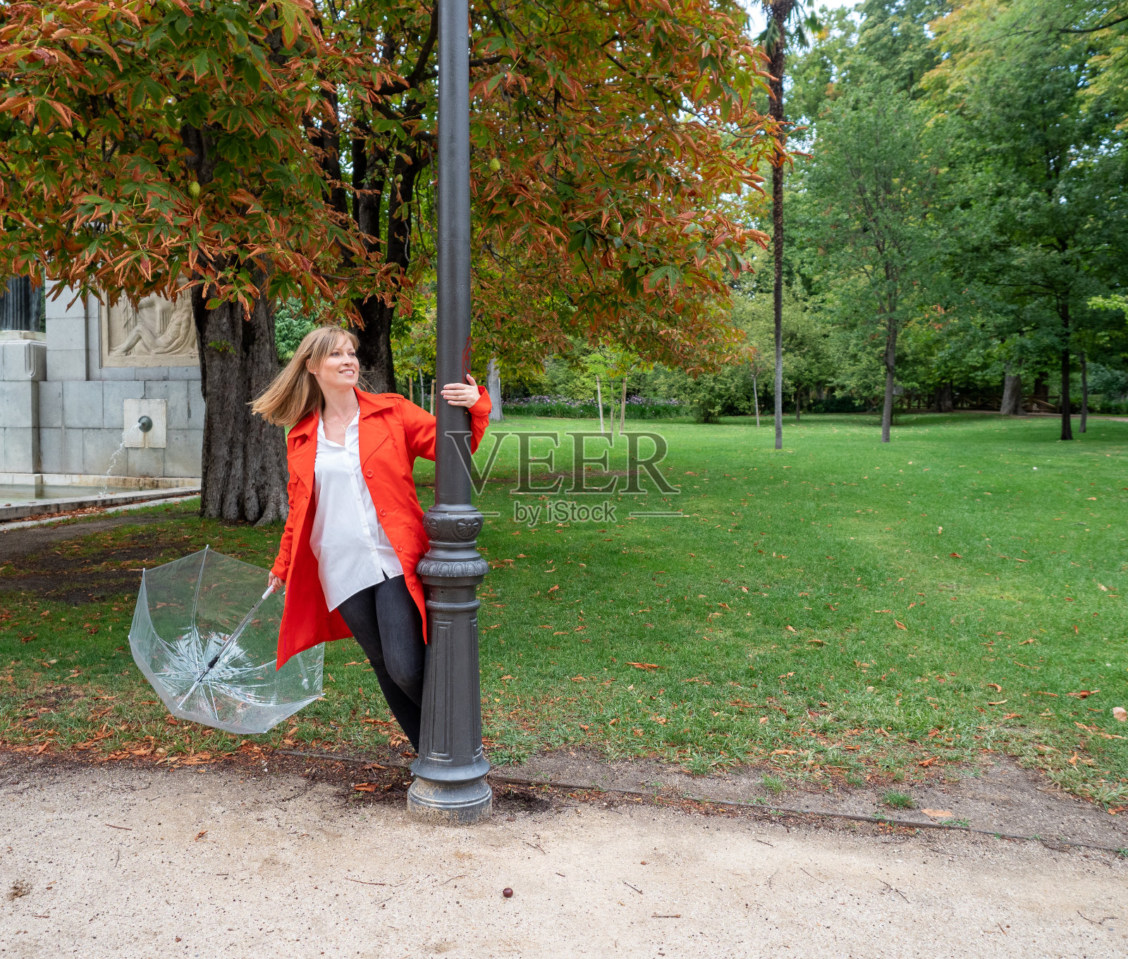 一个身穿红色外套的白人女孩在灯柱旁玩着透明的雨伞照片摄影图片