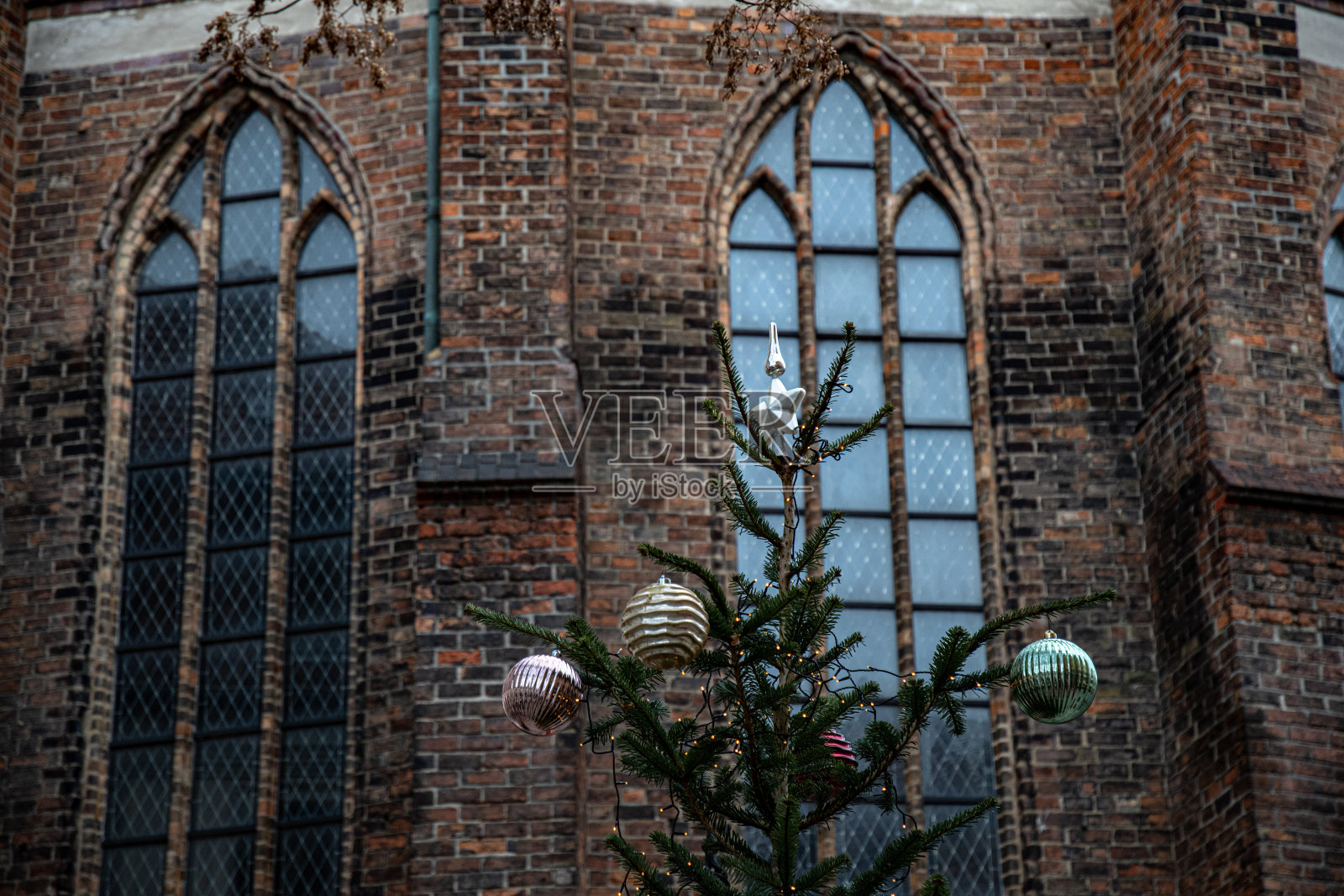 寒假在欧洲。圣诞树上装饰着银色和金色的圣诞饰品,背景是中世纪建筑古老的风化砖墙上哥特式拱形窗户的模糊背景。照片摄影图片