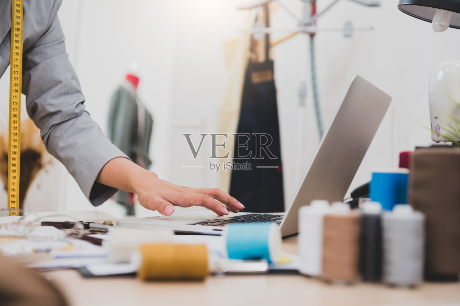 特写女时装设计师手工作在服装店工作室和使用笔记本电脑联系客户。女性创造设计新系列。裁缝缝纫。人们生活方式的概念照片摄影图片