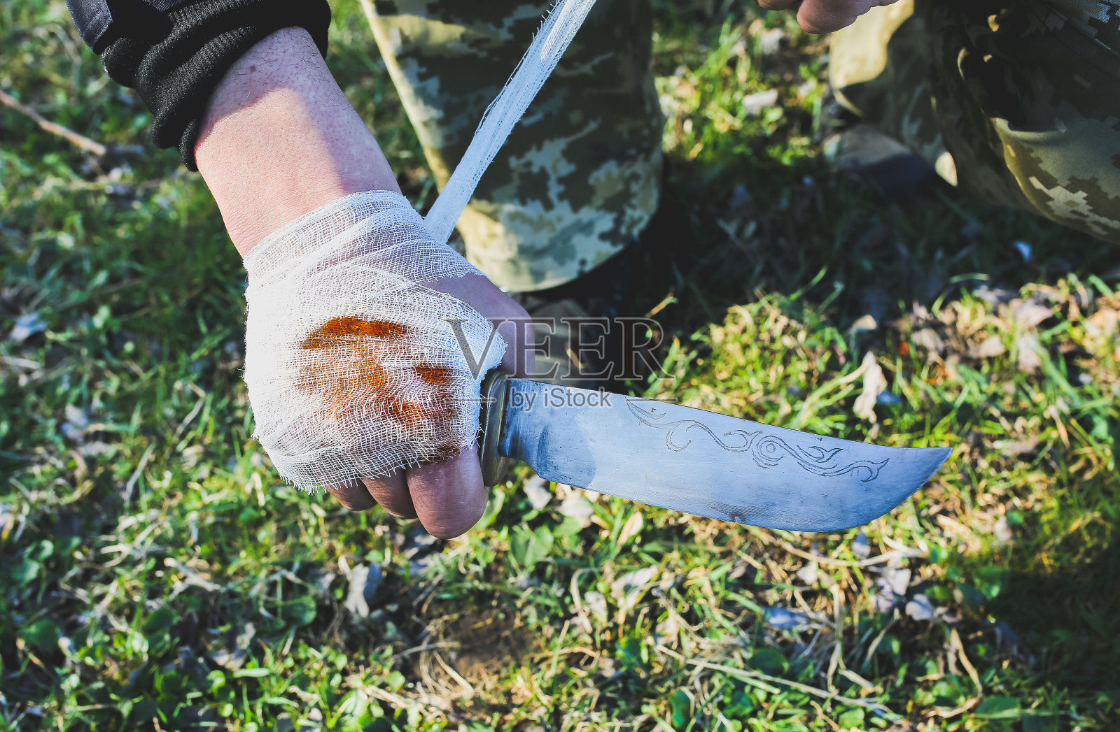 男人正在给流血的伤口包扎。受伤的手。草丛里的刀子。游客在大自然中。感染的危险。治疗。照片摄影图片