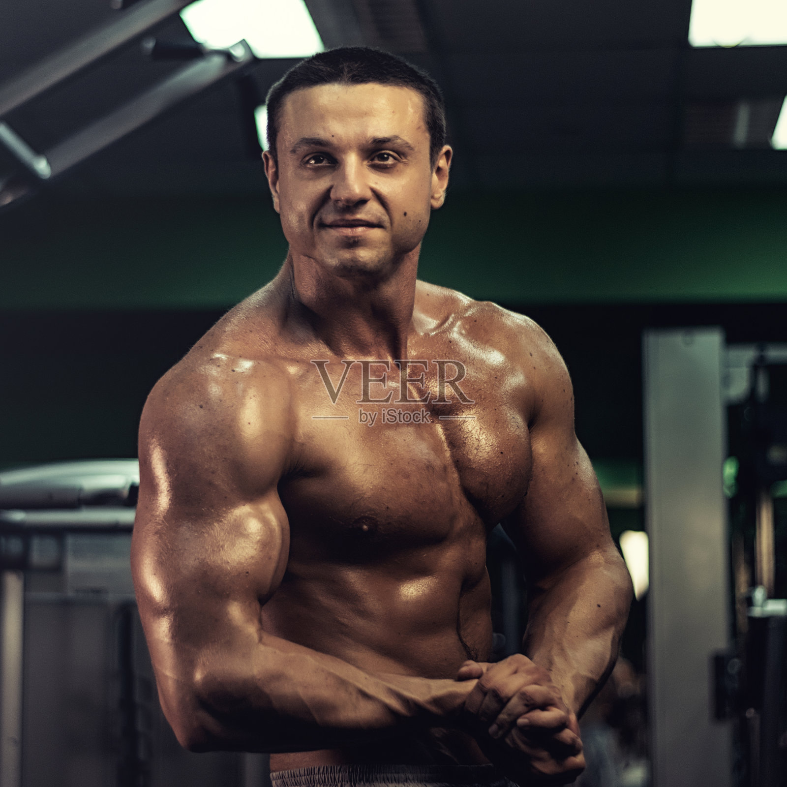 肌肉健美者在健身房的酒吧里做运动。一个英俊的,运动的,性感的家伙在健身房锻炼腹肌。健身,健美,营养,健康的生活方式照片摄影图片