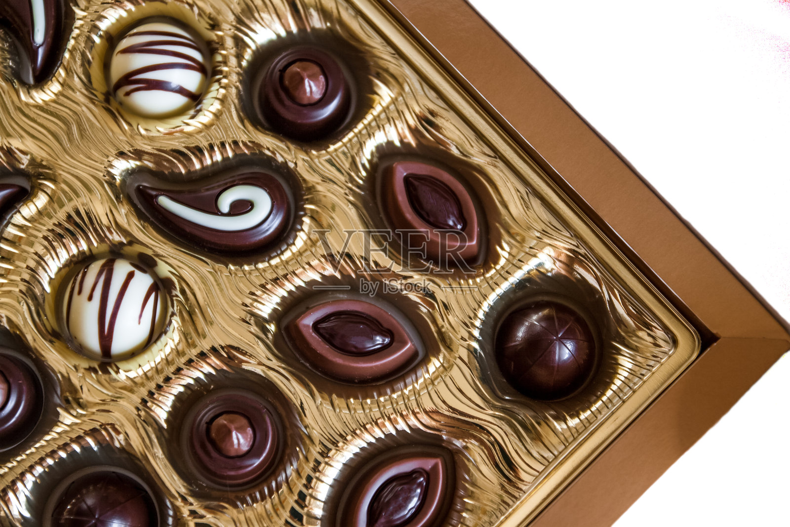 不同形状的巧克力糖果在一个金色的盒子里,从上面看。孤立在白色背景上。特写镜头。照片摄影图片