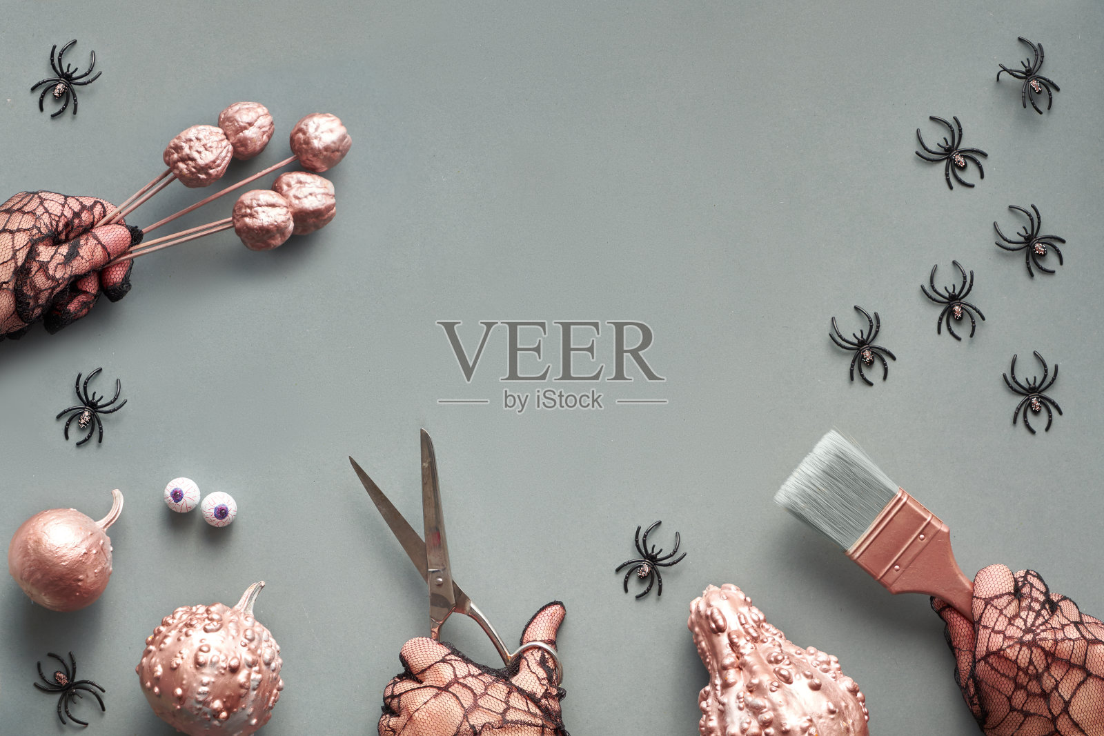 创意万圣节平躺在灰色的纸背景与复制空间。框架的手在黑色网格手套,拿着油漆刷和装饰南瓜。照片摄影图片