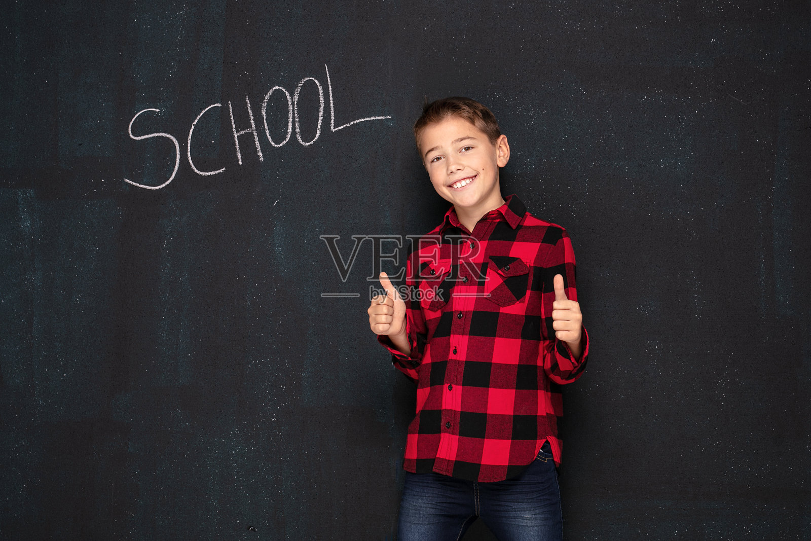 十几岁的男孩穿着格子衬衫在黑色黑板上。照片摄影图片