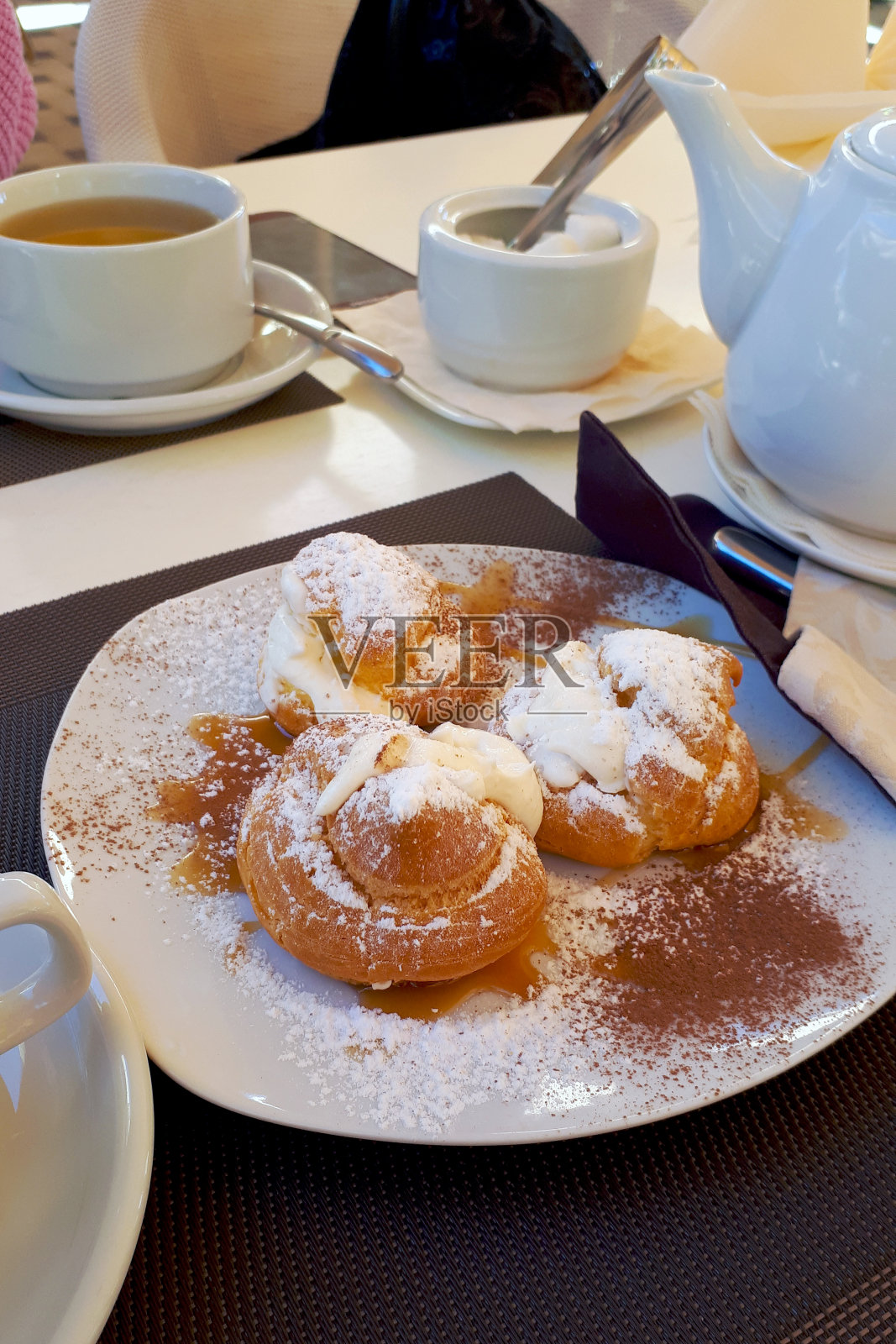 灰色的桌子上放着新鲜的甜酥饼,上面撒着糖粉,旁边是茶壶和茶杯照片摄影图片
