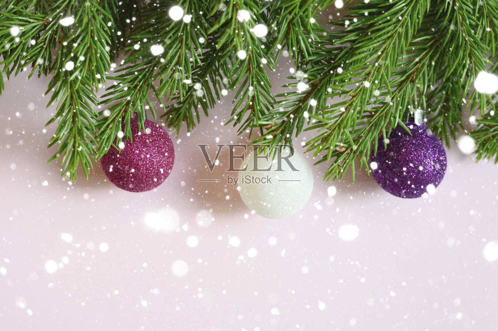 圣诞树的树枝与圣诞装饰品玩具球,框架在粉红色的背景。飘落的雪花照片摄影图片