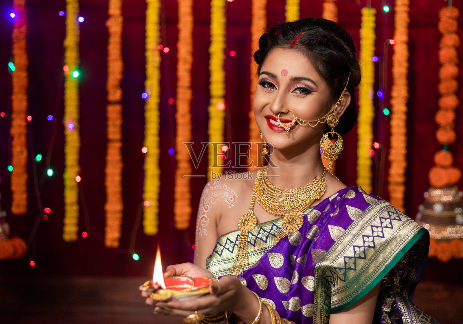 一个美丽的年轻印度妇女的肖像在传统的纱丽服装拿着油灯灯或diya与花的背景在排灯节,工作室肖像照片摄影图片