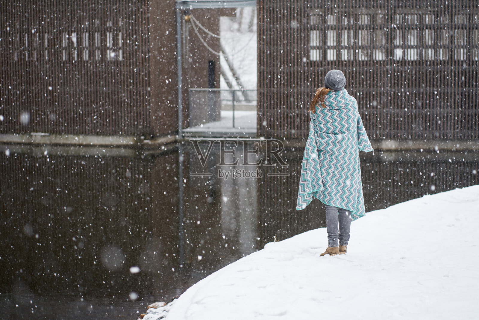 女孩戴着灰色的帽子,穿着蓝色的格子,站在河边欣赏雪花照片摄影图片