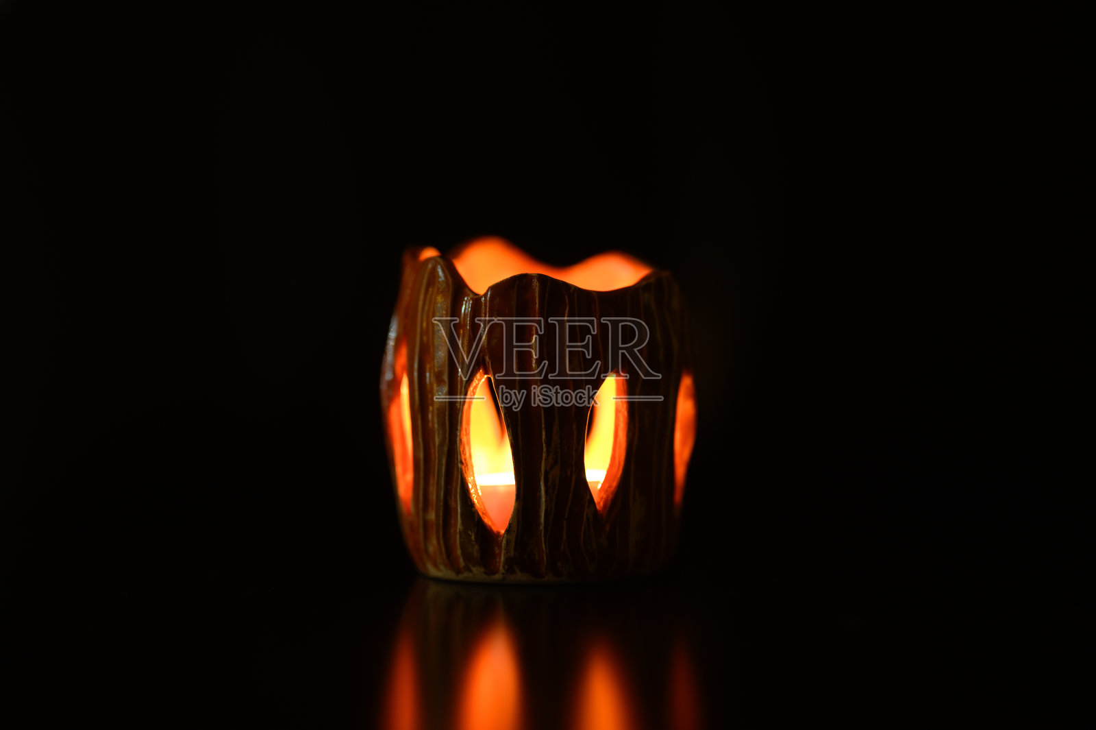 点燃的蜡烛在黑色背景上的烛台内燃烧。美丽的火焰光从蜡烛的狭缝用你自己的手粘土做的烛台。蜡烛发出的眩光被反射了照片摄影图片