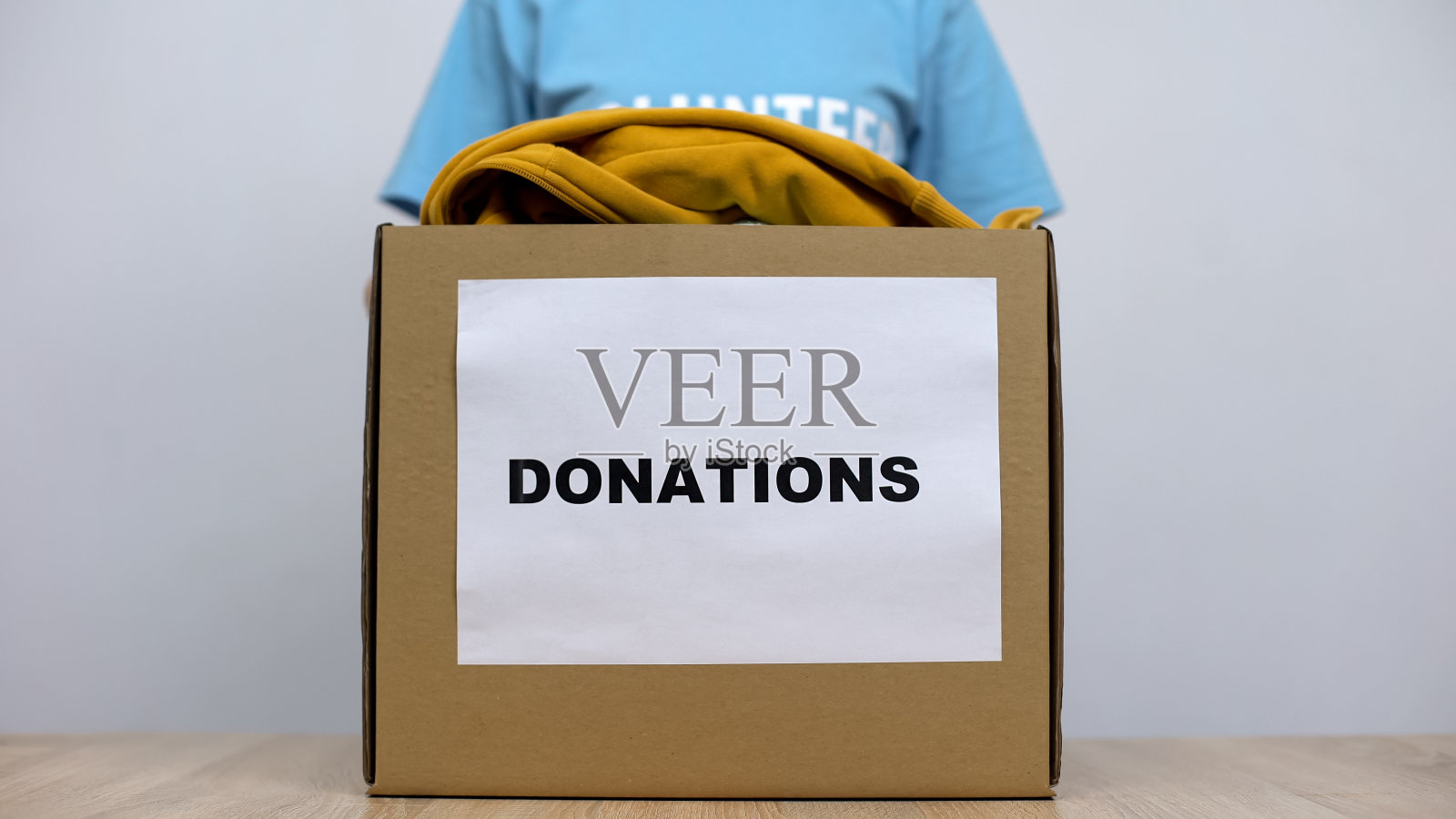 善良的女性活动家站在捐款箱后面,带着衣服,孤儿院的关怀照片摄影图片