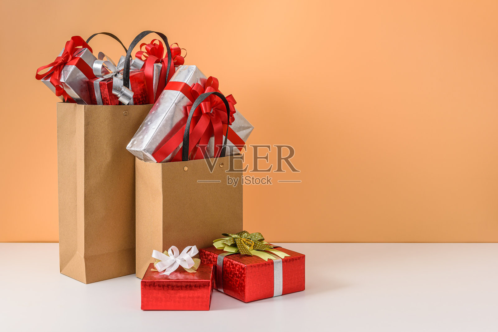 许多礼盒与红色丝带蝴蝶结在棕色纸袋购物。概念新年礼物或圣诞节照片摄影图片