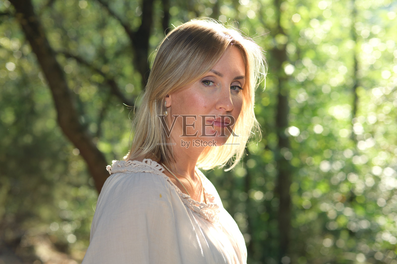 一个女人站在森林里看着摄像机,她的头发被阳光照得亮闪闪的照片摄影图片