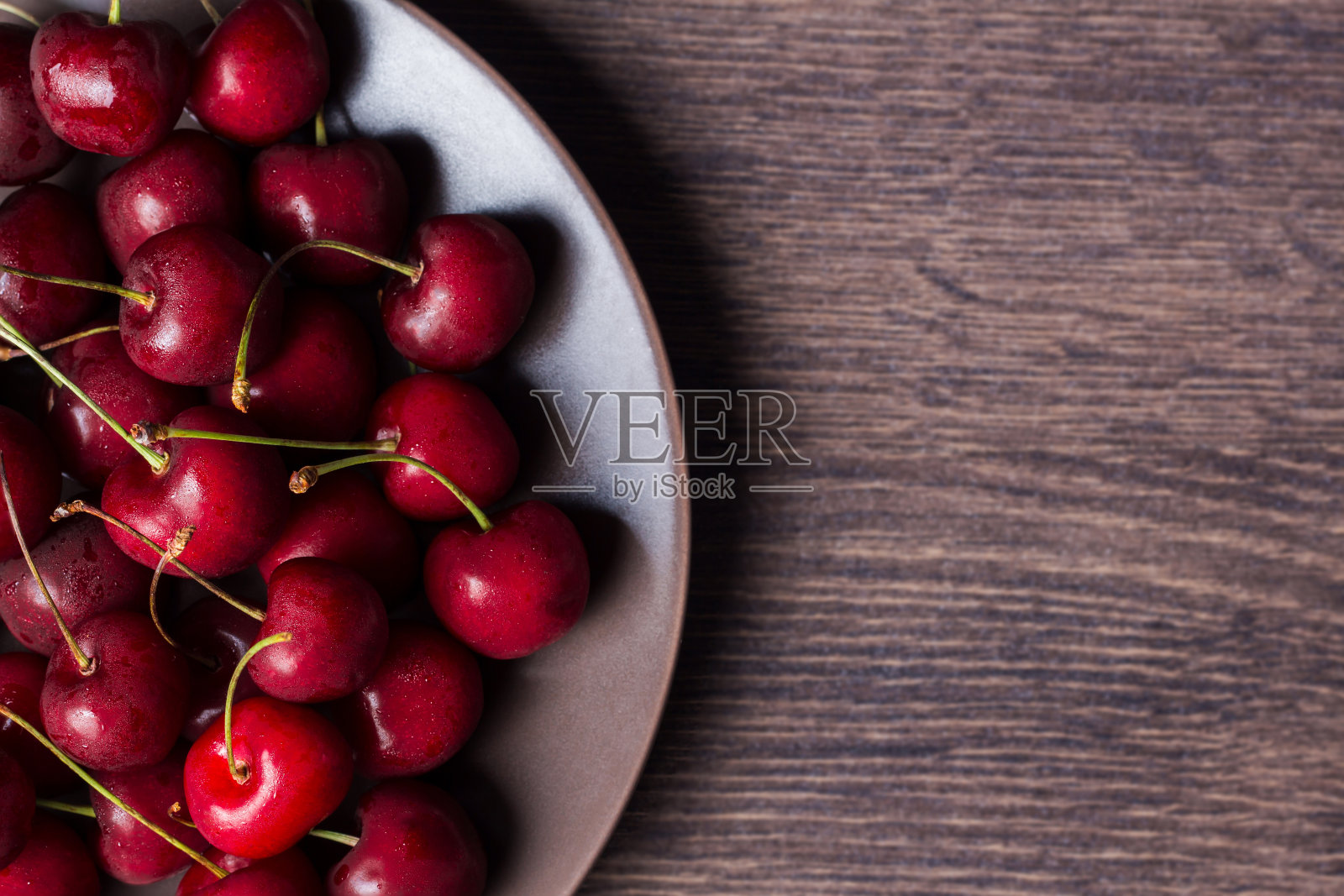 棕色盘子里的樱桃。食物和复印空间放在一张木桌上。浆果,零食,健康食品。素食主义者,素食者,糖尿病患者,水果。照片摄影图片