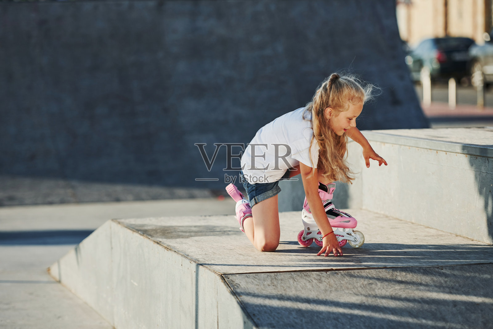 可爱的小女孩穿着溜冰鞋坐在户外的坡道上进行极限运动照片摄影图片