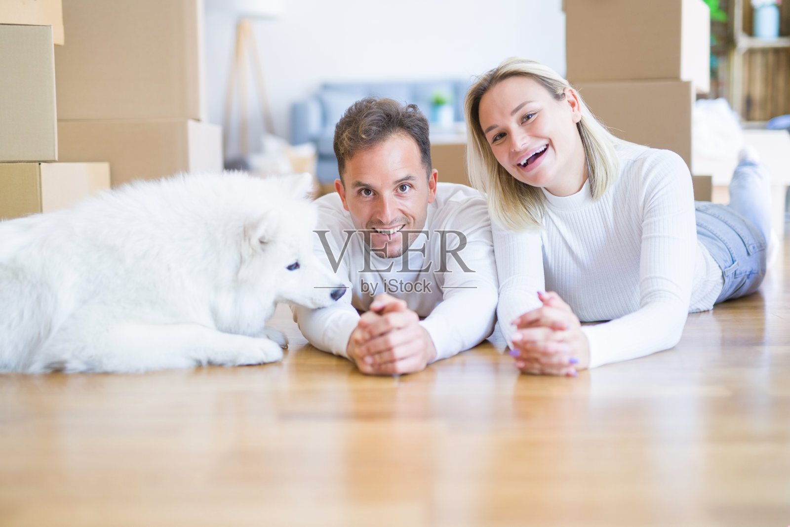 年轻美丽的夫妇和狗躺在地板上的新家周围的纸箱照片摄影图片