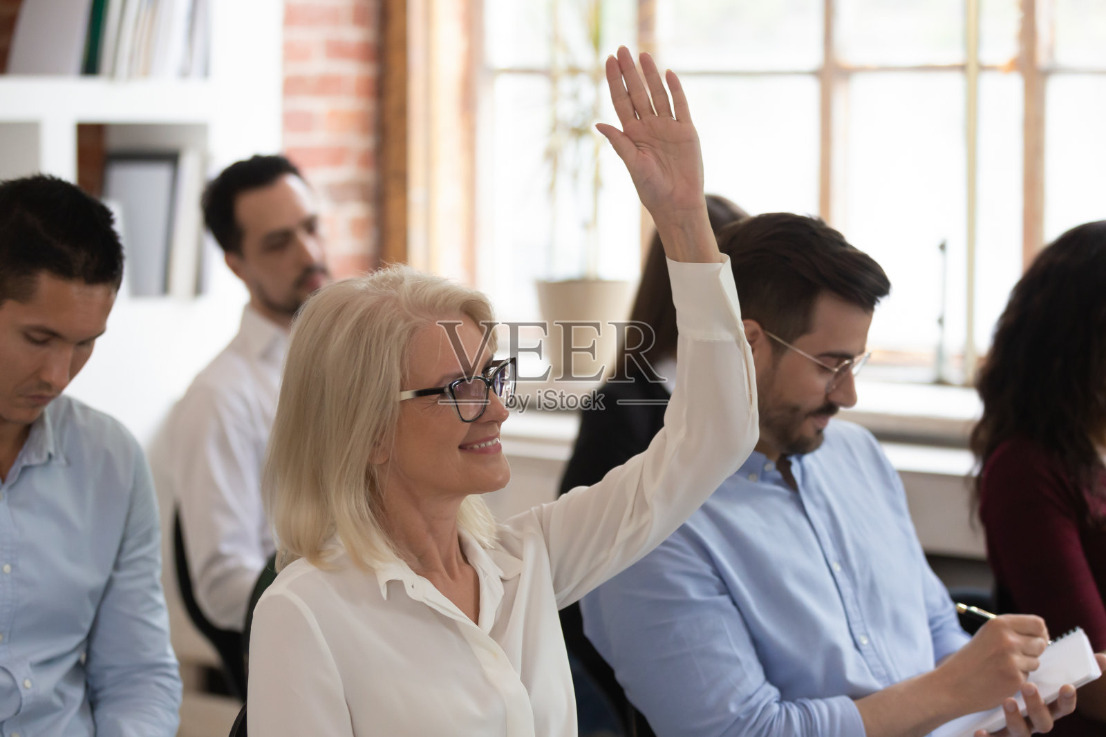 研讨会上举手提问的中年妇女照片摄影图片
