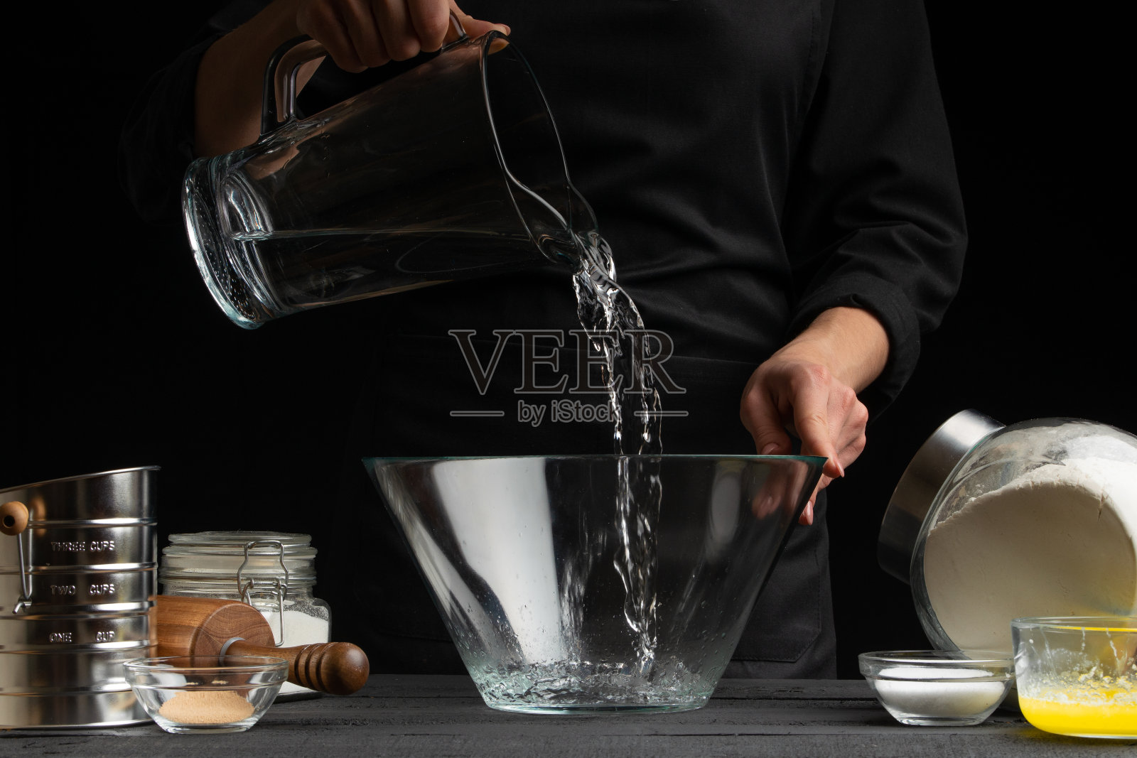 厨师为意大利面、披萨、面包和面包卷制作面团,将水倒进容器中,在运动中冻结。在黑色背景,水平照片照片摄影图片