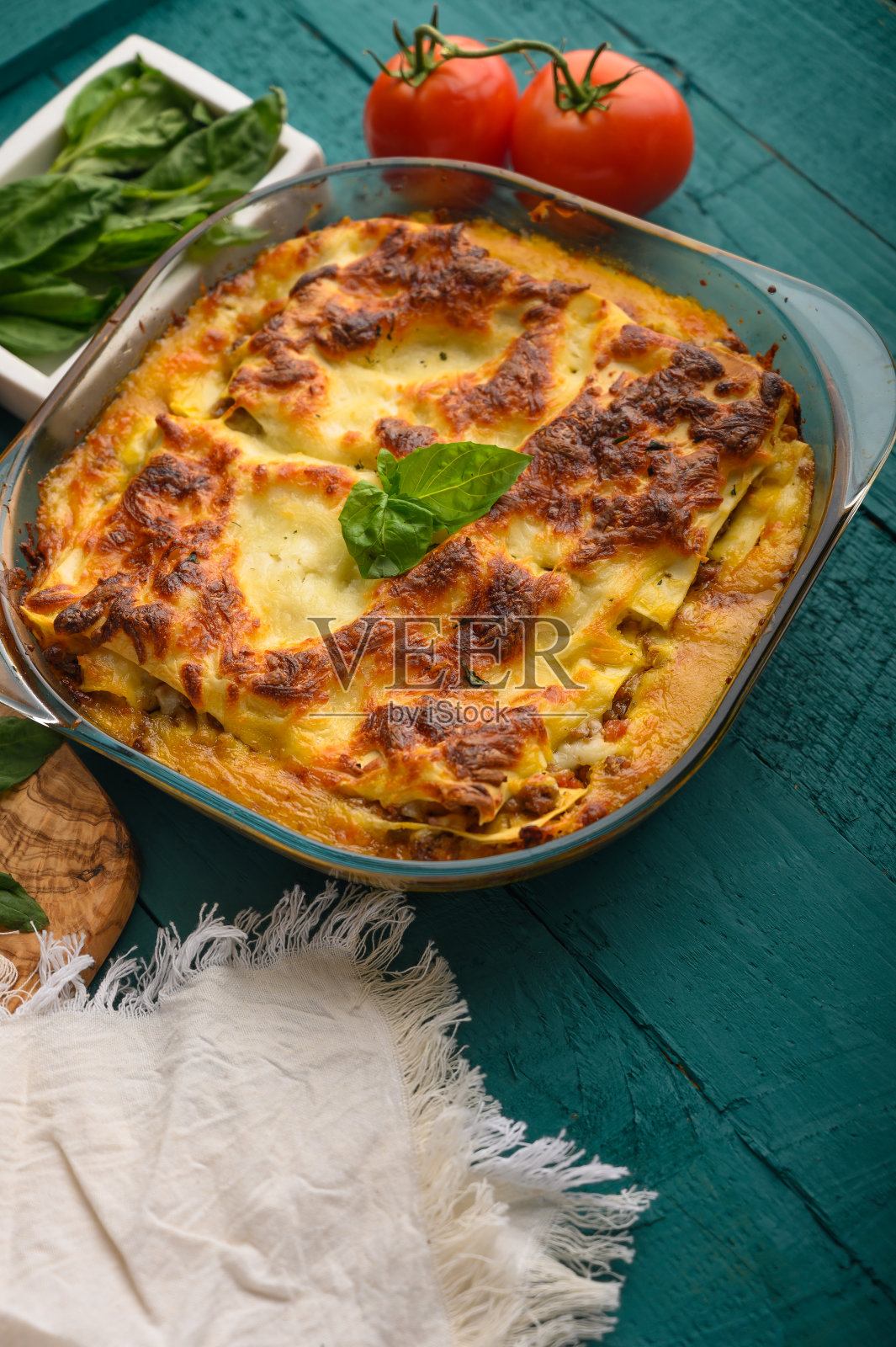 准备好的意大利千层面,在绿色的木质背景上放上罗勒和番茄。烹饪背景,意大利食谱,美味的食物。垂直框架照片摄影图片