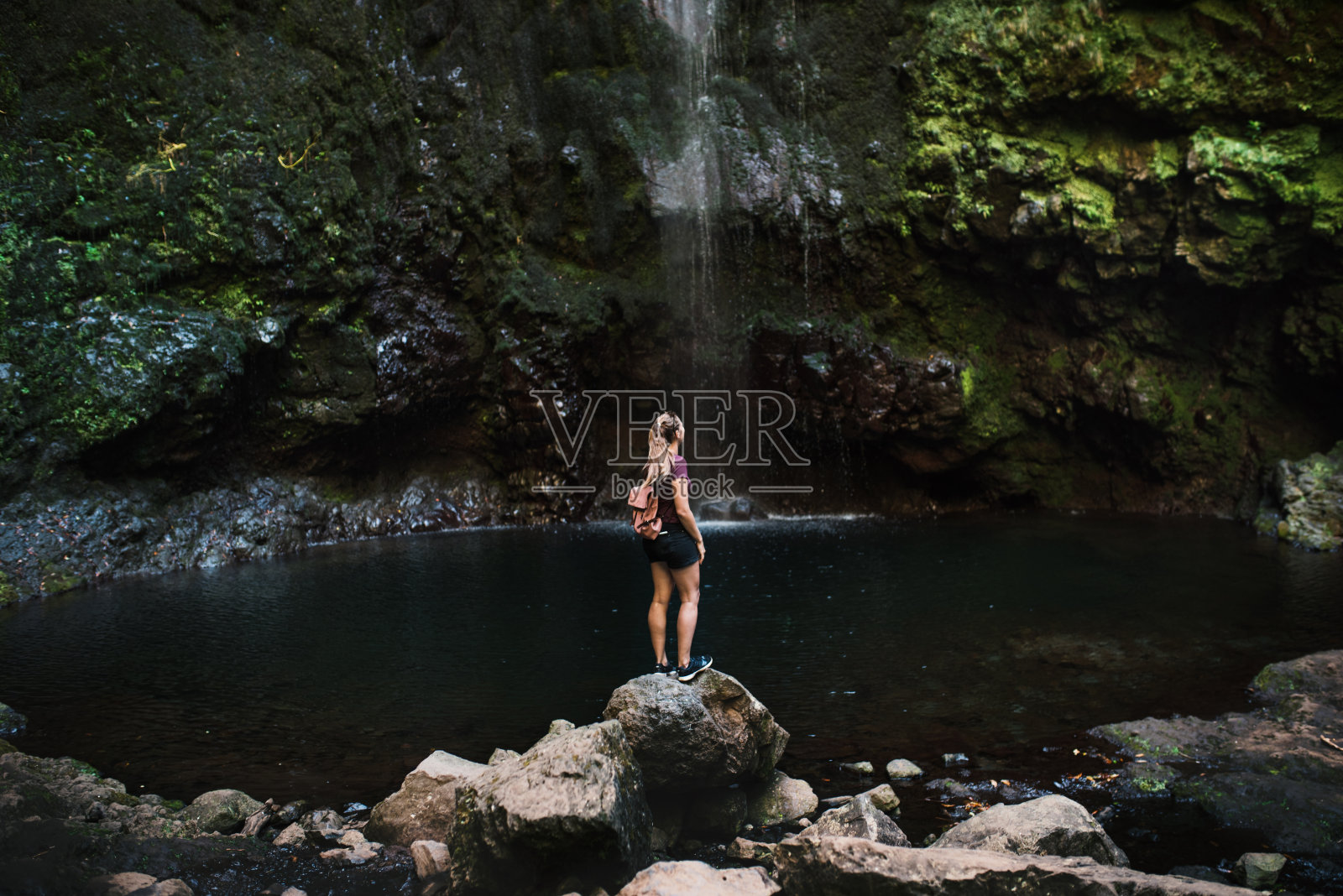 葡萄牙马德拉美丽的森林。年轻的旅行者靠着瀑布站着。照片摄影图片