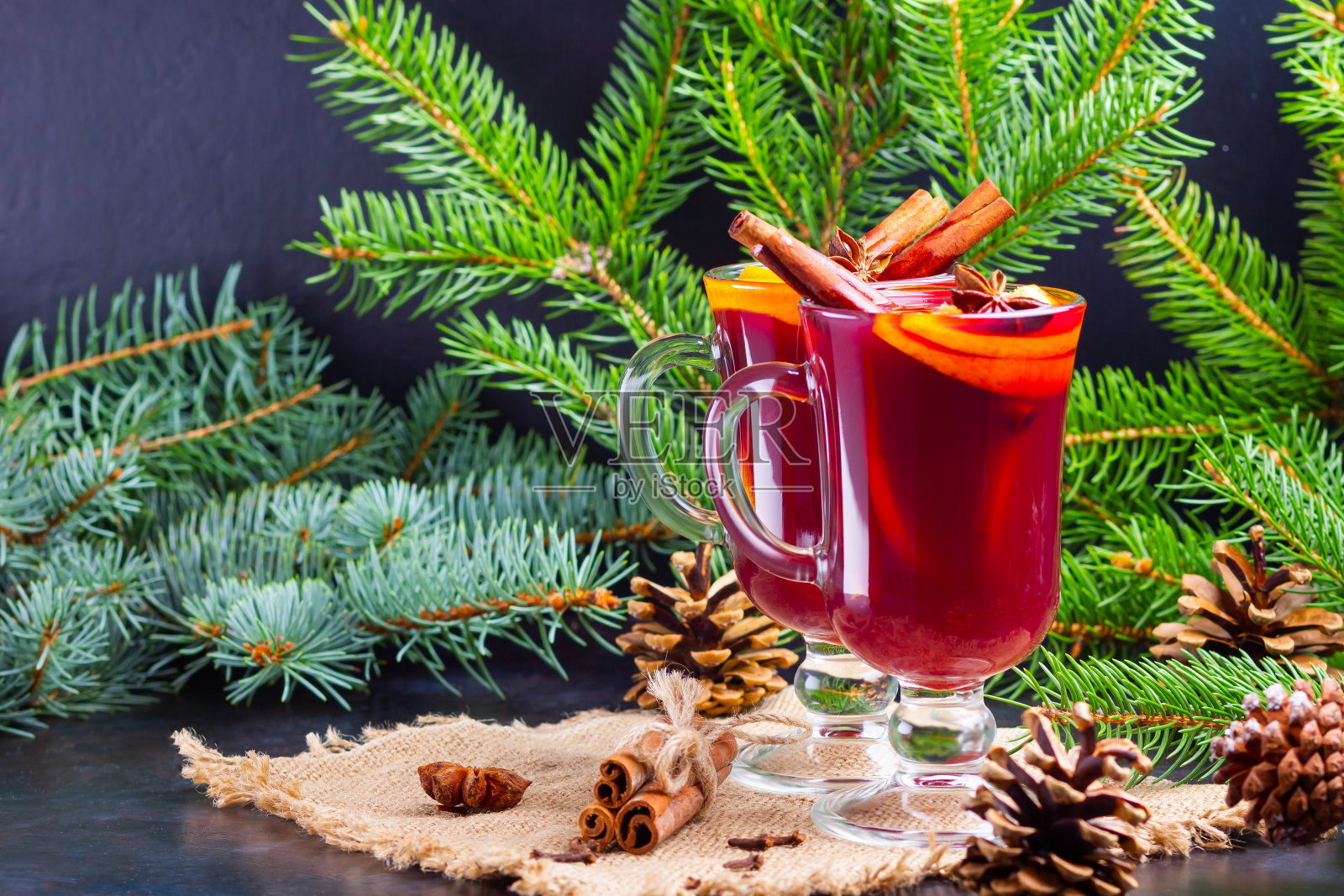 热红酒和粗麻布上的冷杉树枝。橘子,蜂蜜,肉桂和丁香的热葡萄酒在黑暗的背景。加了蜂蜜和香料的热饮照片摄影图片