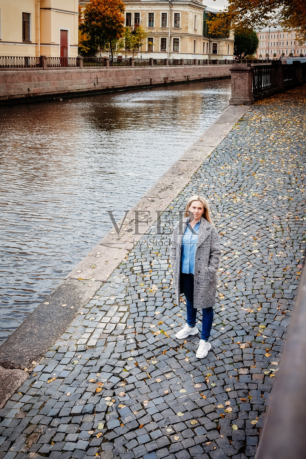 一名年轻女子在一个阳光明媚的秋天沿着圣彼得堡运河散步的肖像照片摄影图片