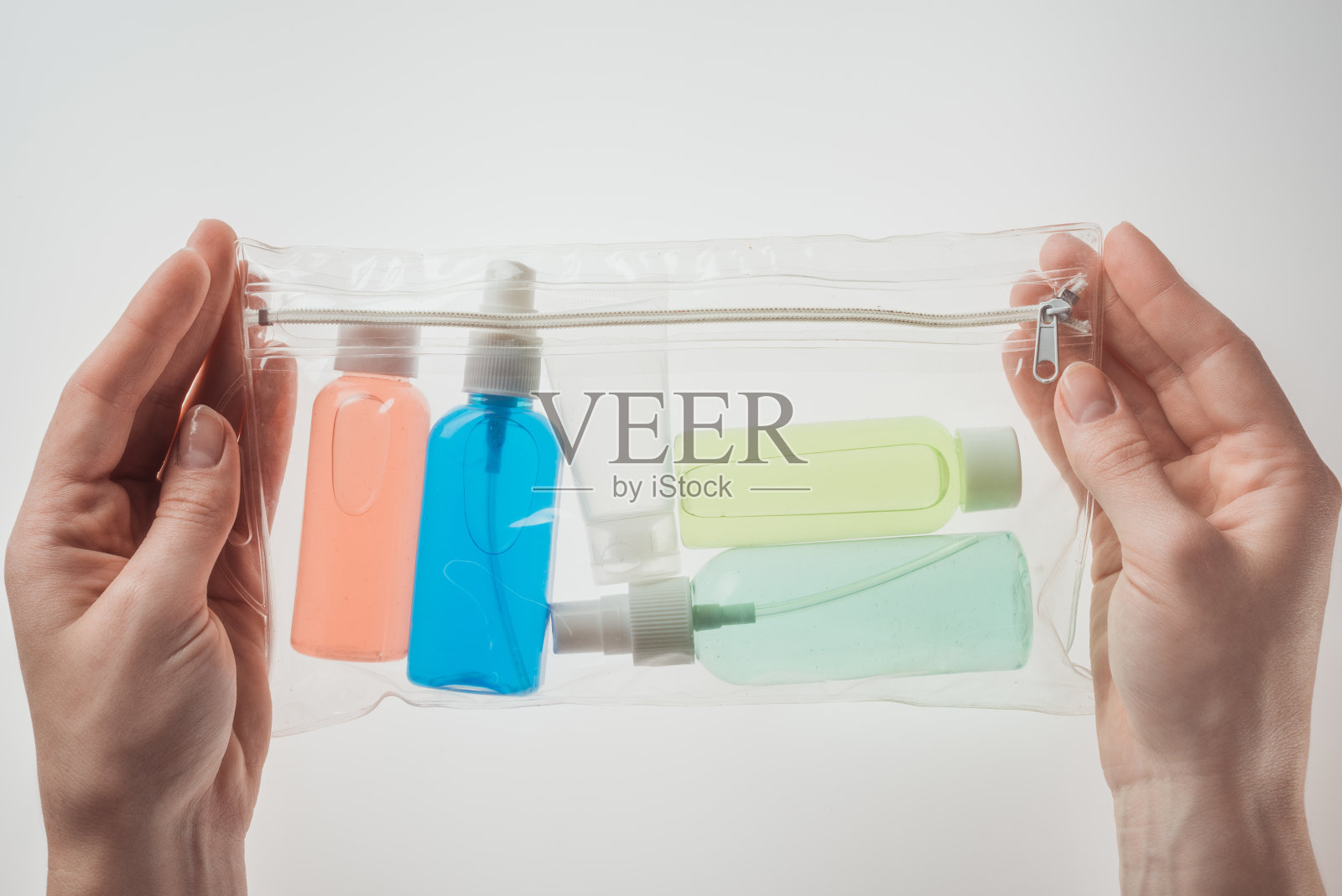 女性抱着彩色瓶子的化妆品袋与液体在白色的背景裁剪的观点照片摄影图片