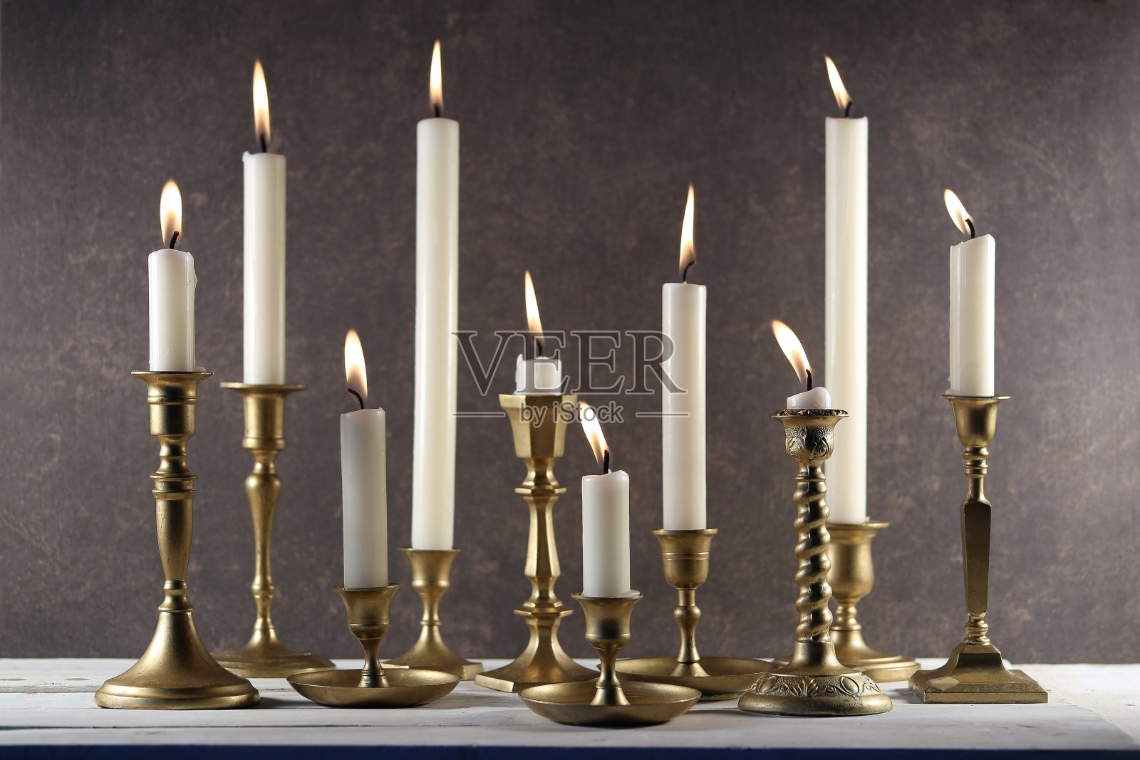 白色木桌上的老式金属烛台上燃烧着蜡烛,背景是黑色的石头。照片摄影图片