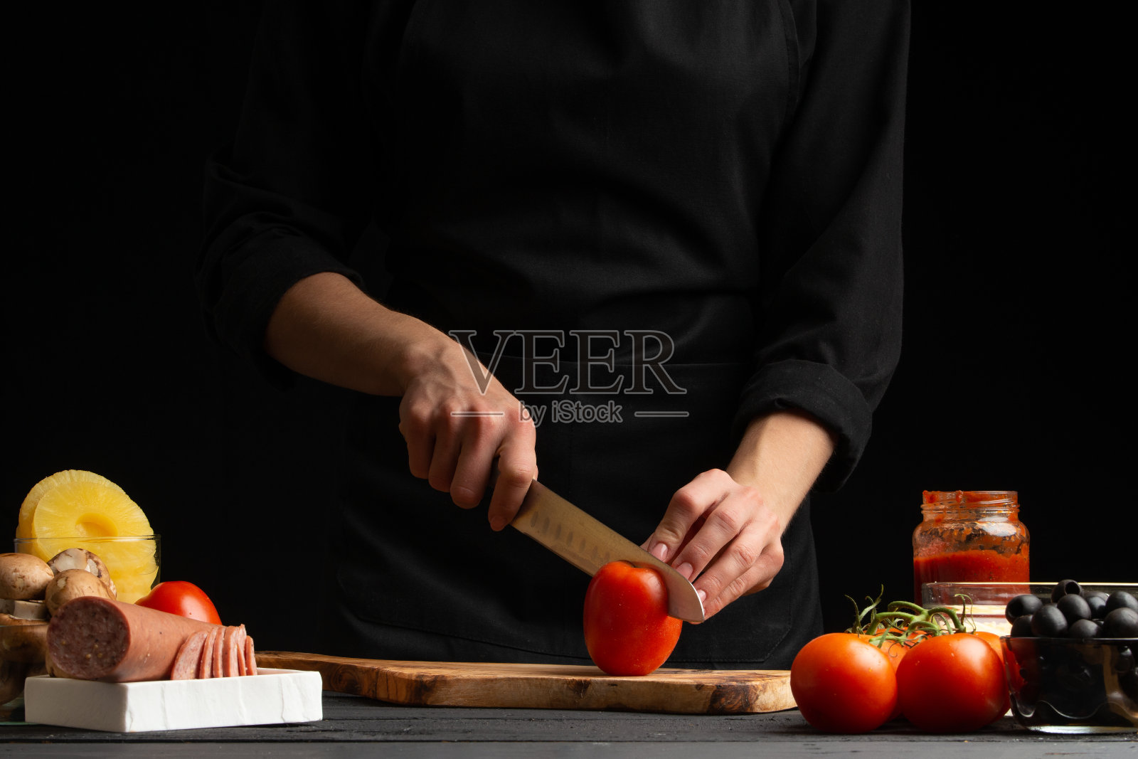 厨师烹制披萨,将新鲜的番茄切片,在背景上配上配料。食谱,菜单,家常菜。横向框架。照片摄影图片