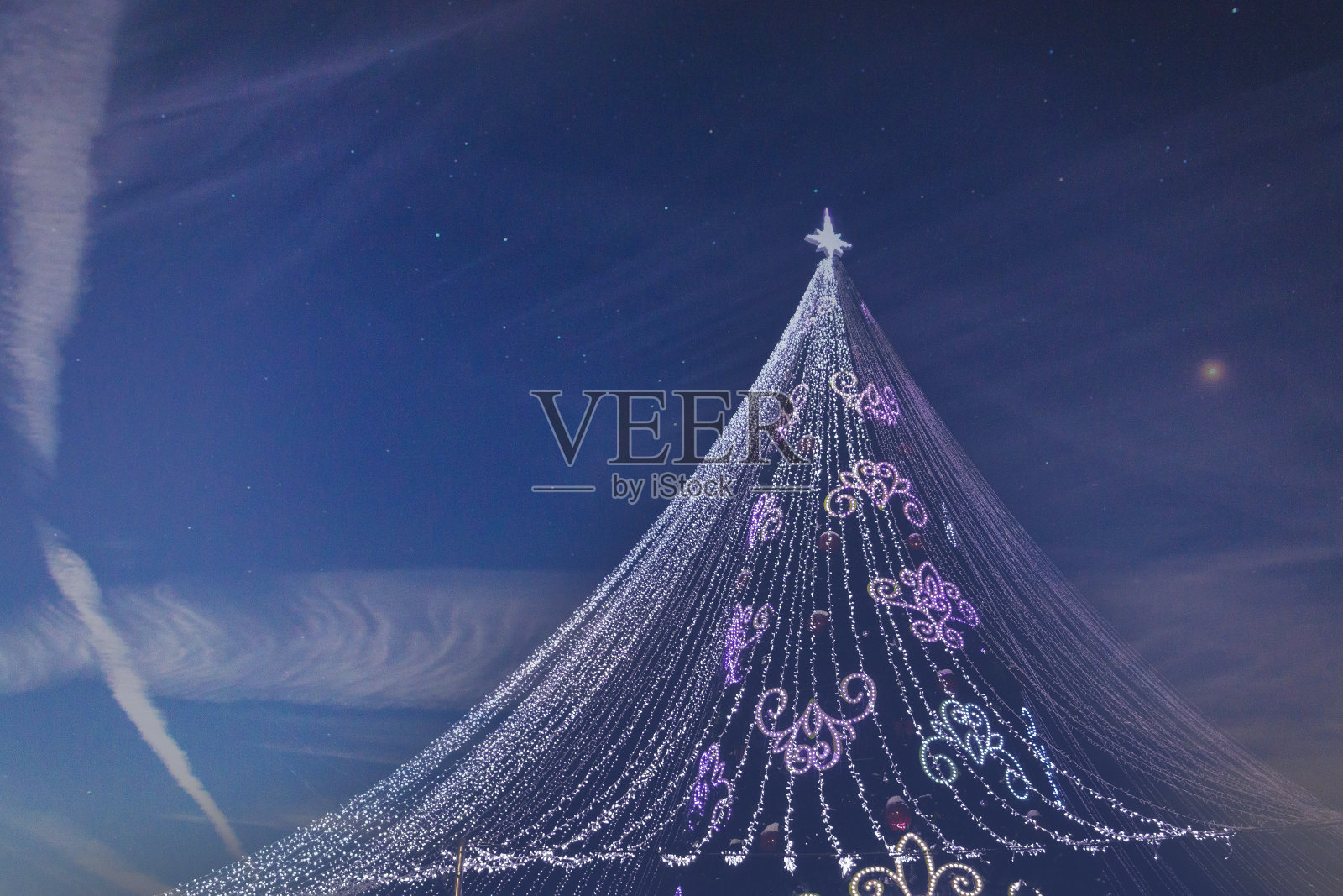 白雪覆盖的圣诞树与多彩灯在晚上。在星空的背景下,圣诞节,新年,假期。照片摄影图片