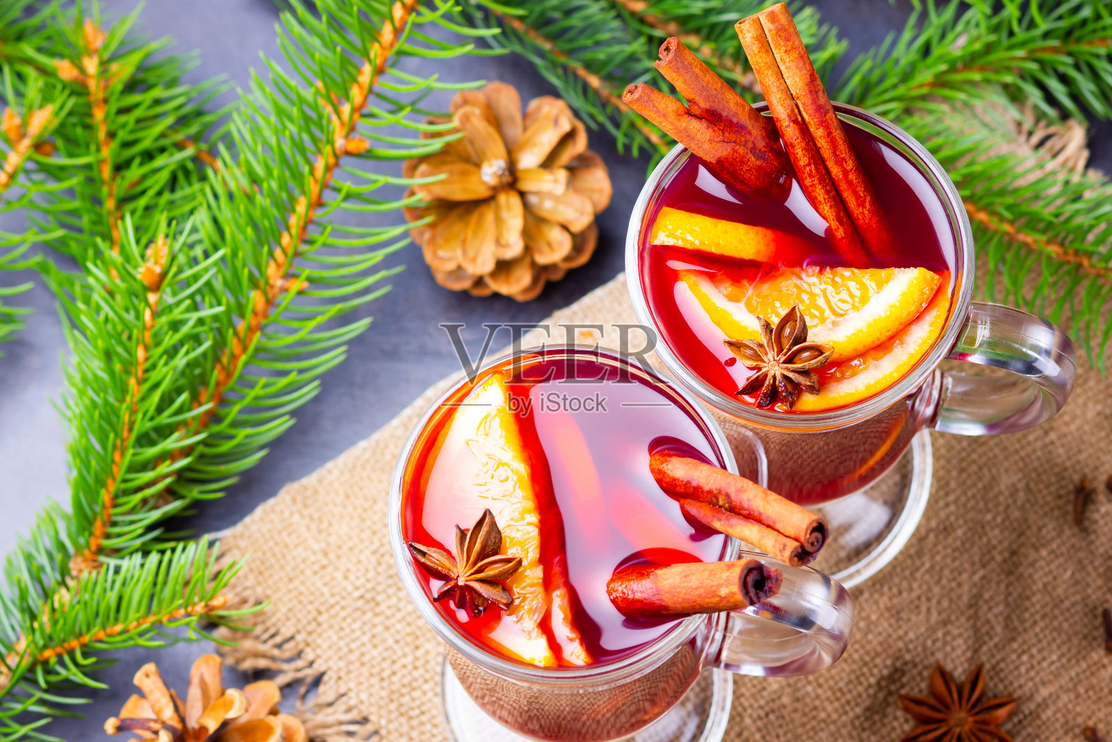 热红酒和粗麻布上的冷杉树枝。橘子,蜂蜜,肉桂和丁香的热葡萄酒在黑暗的背景。加了蜂蜜和香料的热饮照片摄影图片
