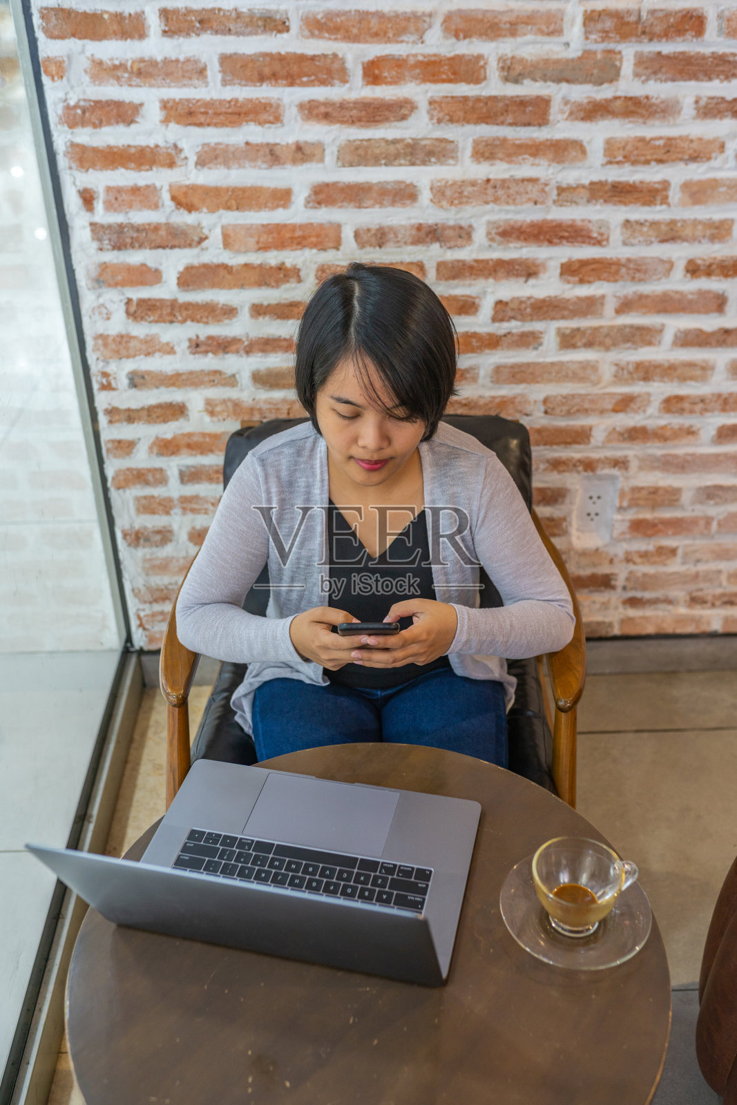 亚洲女性坐在笔记本电脑前看智能手机屏幕照片摄影图片