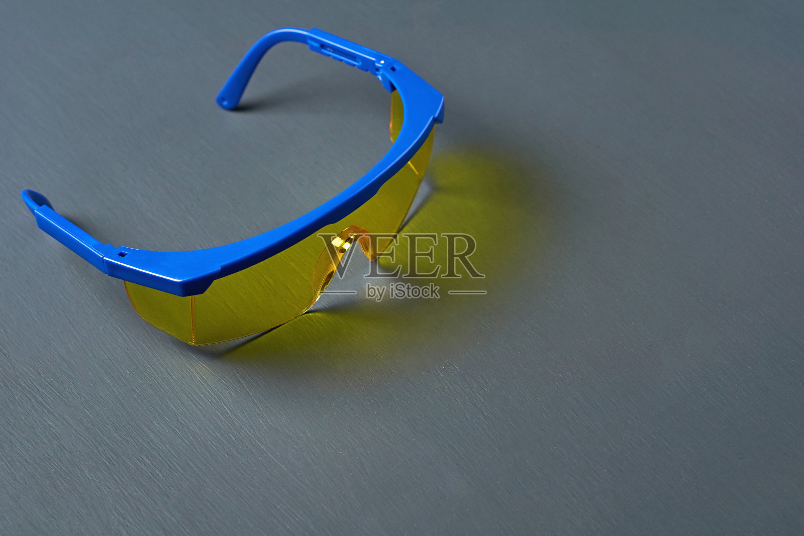 黑色的混凝土桌子上放着一副滑雪镜或现代防护眼镜,适合建筑工人、焊工、牙医、turner等工作人员戴,玻璃黄色,镜框蓝色。空间的文本照片摄影图片