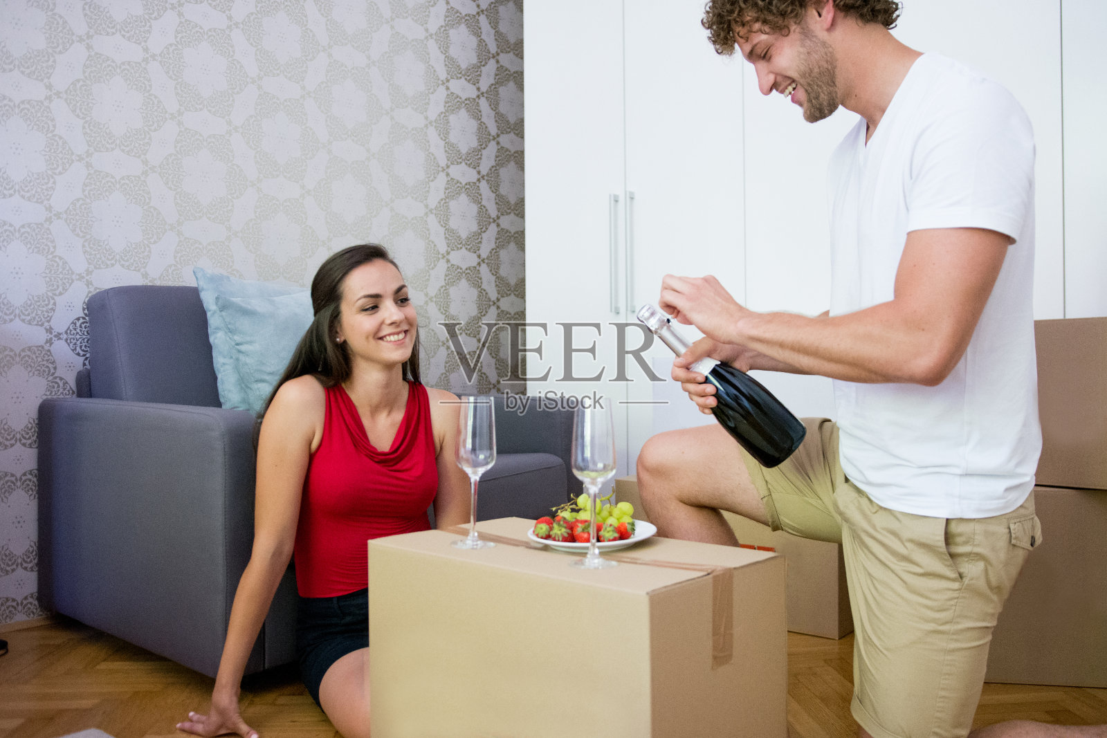 一对年轻的异性恋夫妇坐在新房子的地板上喝着香槟照片摄影图片