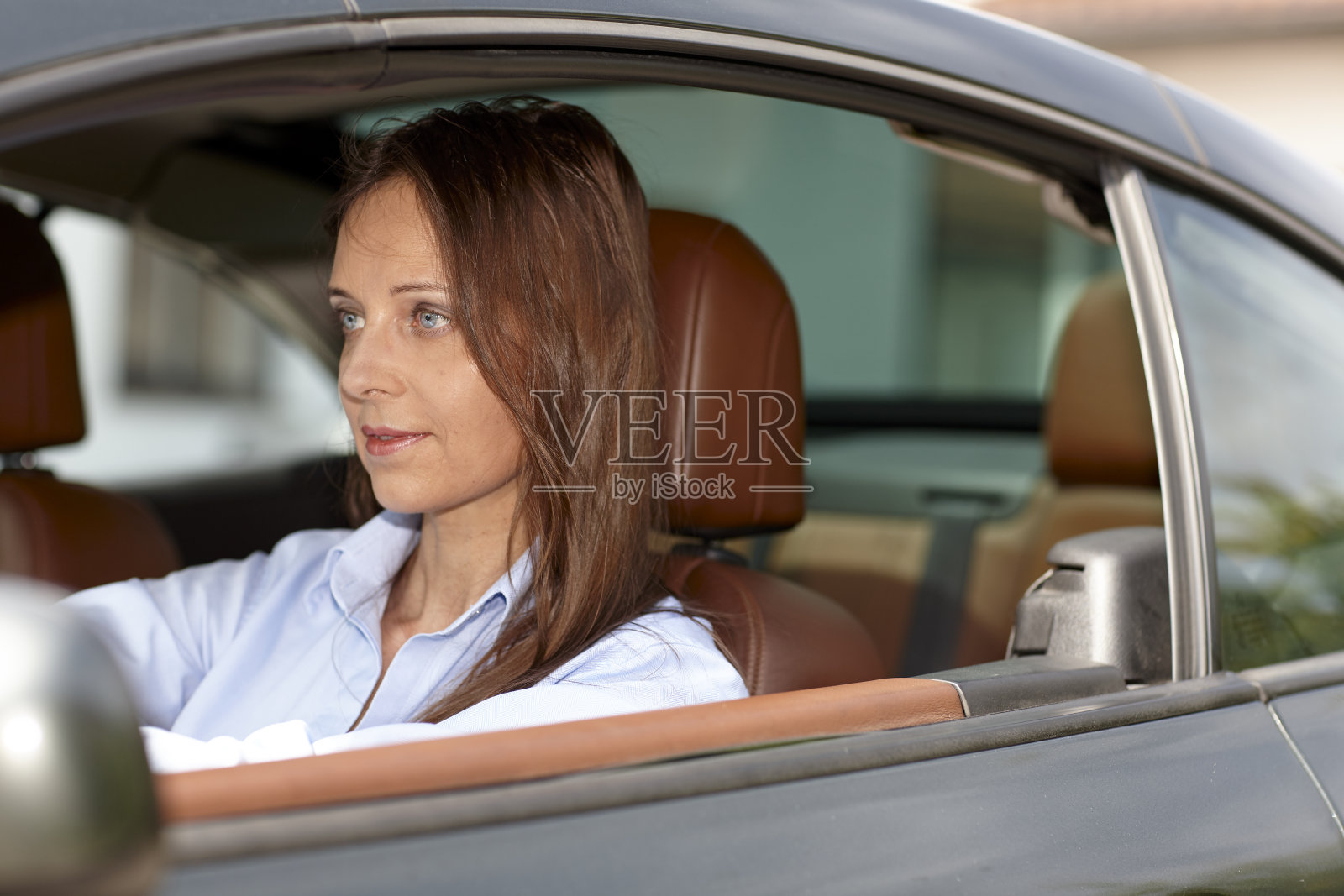 棕色长发、蓝色衬衫的成熟女人正坐在车里开车照片摄影图片