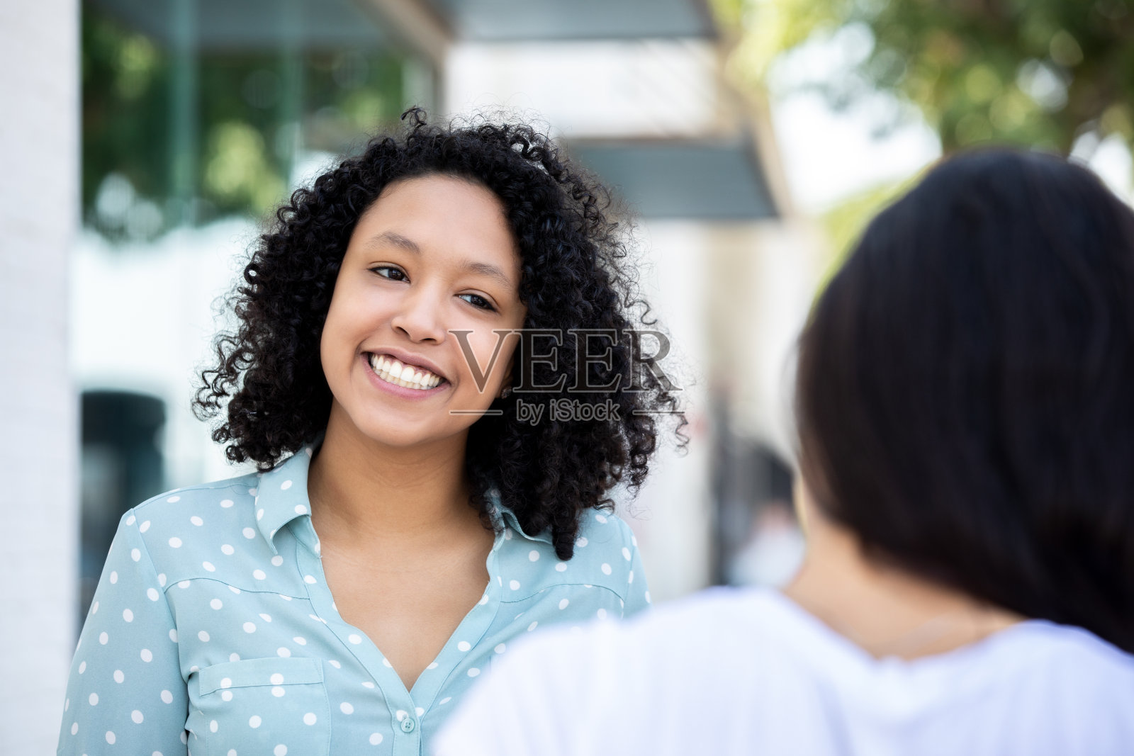 美丽的年轻女子卷头发和朋友在户外交谈照片摄影图片