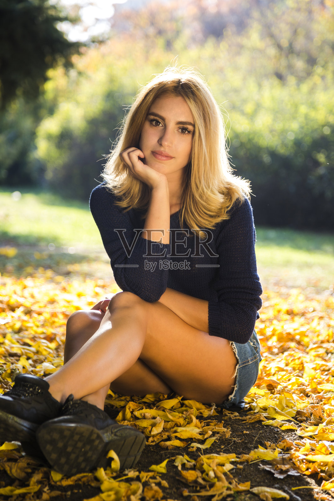 秋天的季节。一个穿着蓝毛衣的女人在玩树叶的肖像照片摄影图片