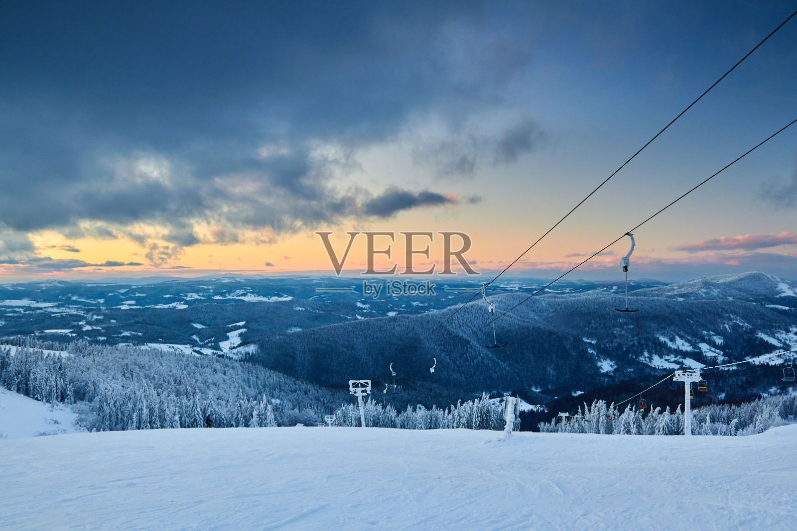 傍晚的冬季景观在山上与杉树林日落。大雪过后,山被雪覆盖了。雪野滑雪场景色。壮观的云彩在日出时出现在地平线上照片摄影图片