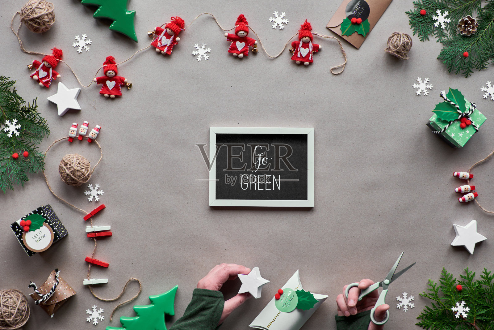 创意手工装饰,零浪费圣诞框架。平铺,牛皮纸俯视图。纺织品小饰品,手拿装饰好的纸盒。生态友好的圣诞节。在黑板上写“Go green”。照片摄影图片