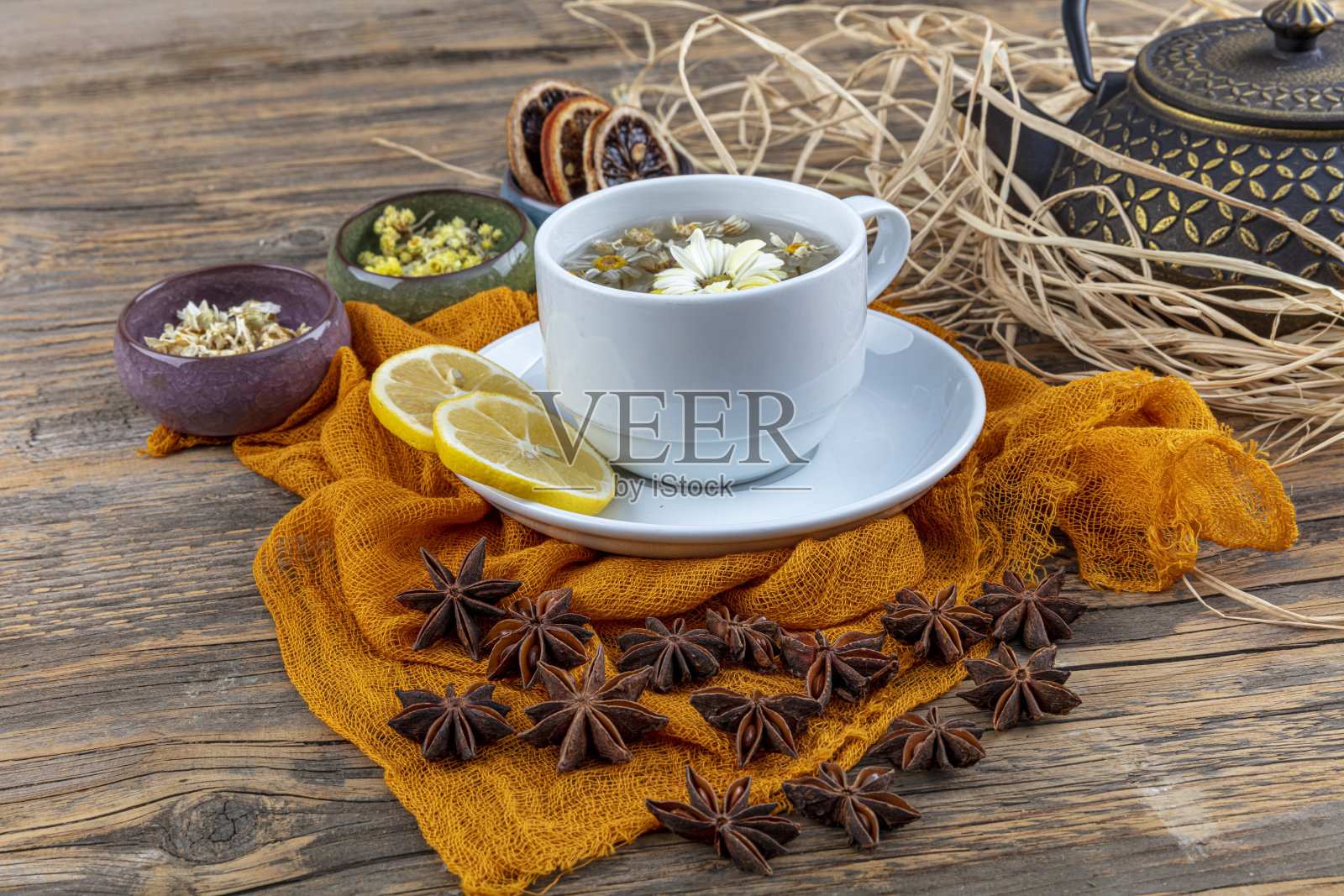 铸造茶壶中的甘菊茶。洋甘菊茶杯,中国古代铸铁茶壶,柠檬和八角放在木桌上。照片摄影图片