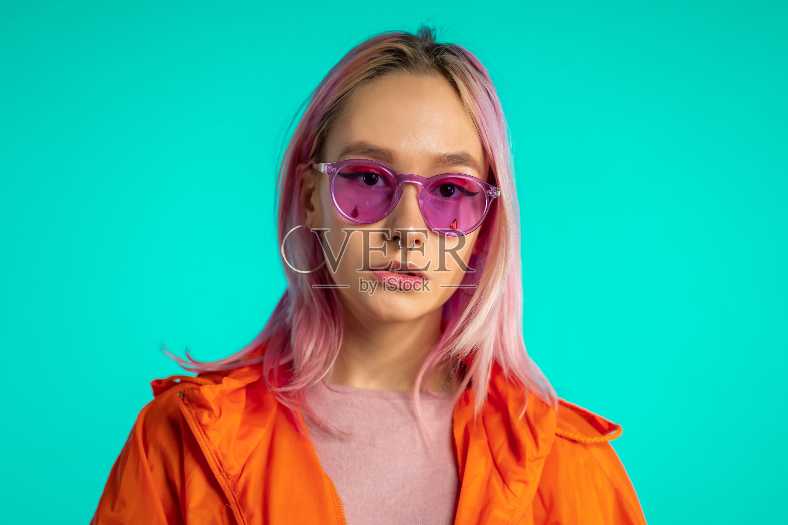 千禧年神秘的漂亮女孩与不寻常的粉红色染发型。金色的亮片如泪珠,刺穿鼻子。蓝色背景下的神秘潮人少年。照片摄影图片