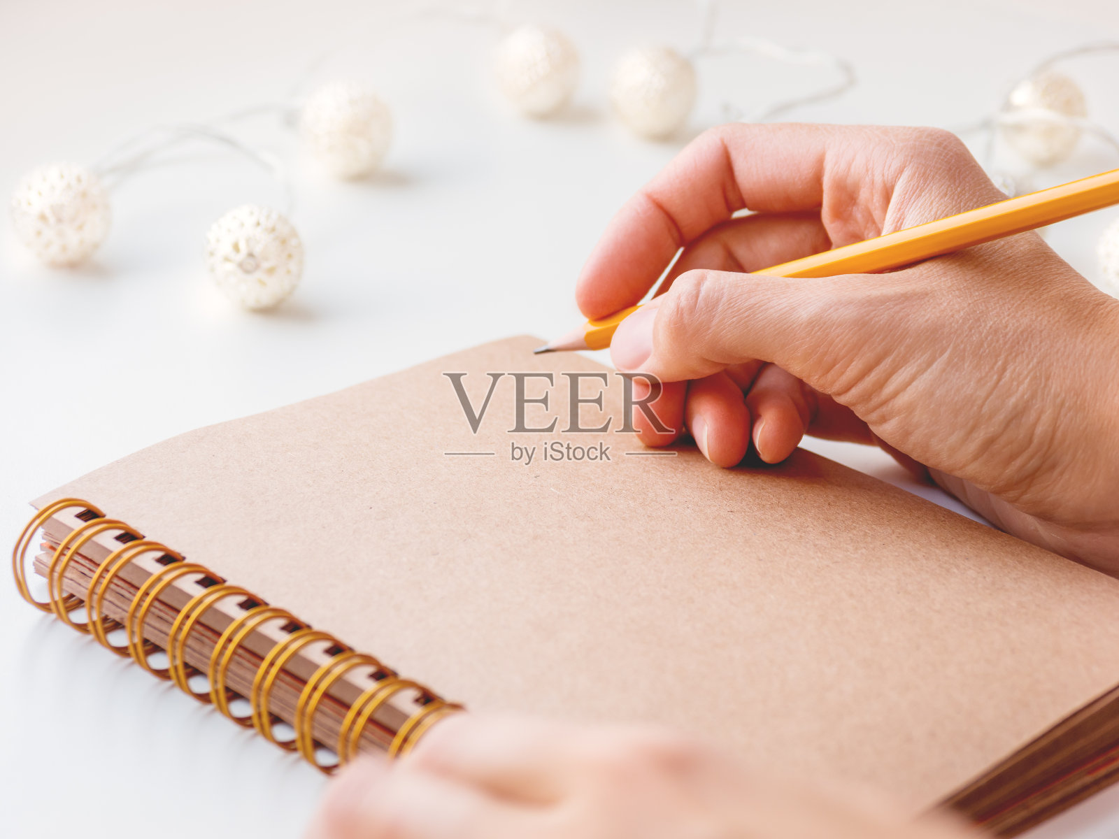 女人正准备写或画一些东西在记事本与牛皮纸页。背景上有灯泡。照片摄影图片