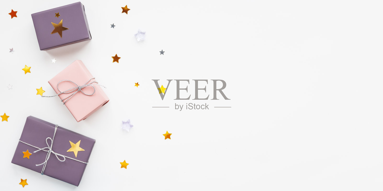 横幅上挂着节日礼物。礼物用淡粉色和紫色的纸包着,还有银色的丝带和蝴蝶结。星星、五彩纸屑和白色的拷贝空间。照片摄影图片